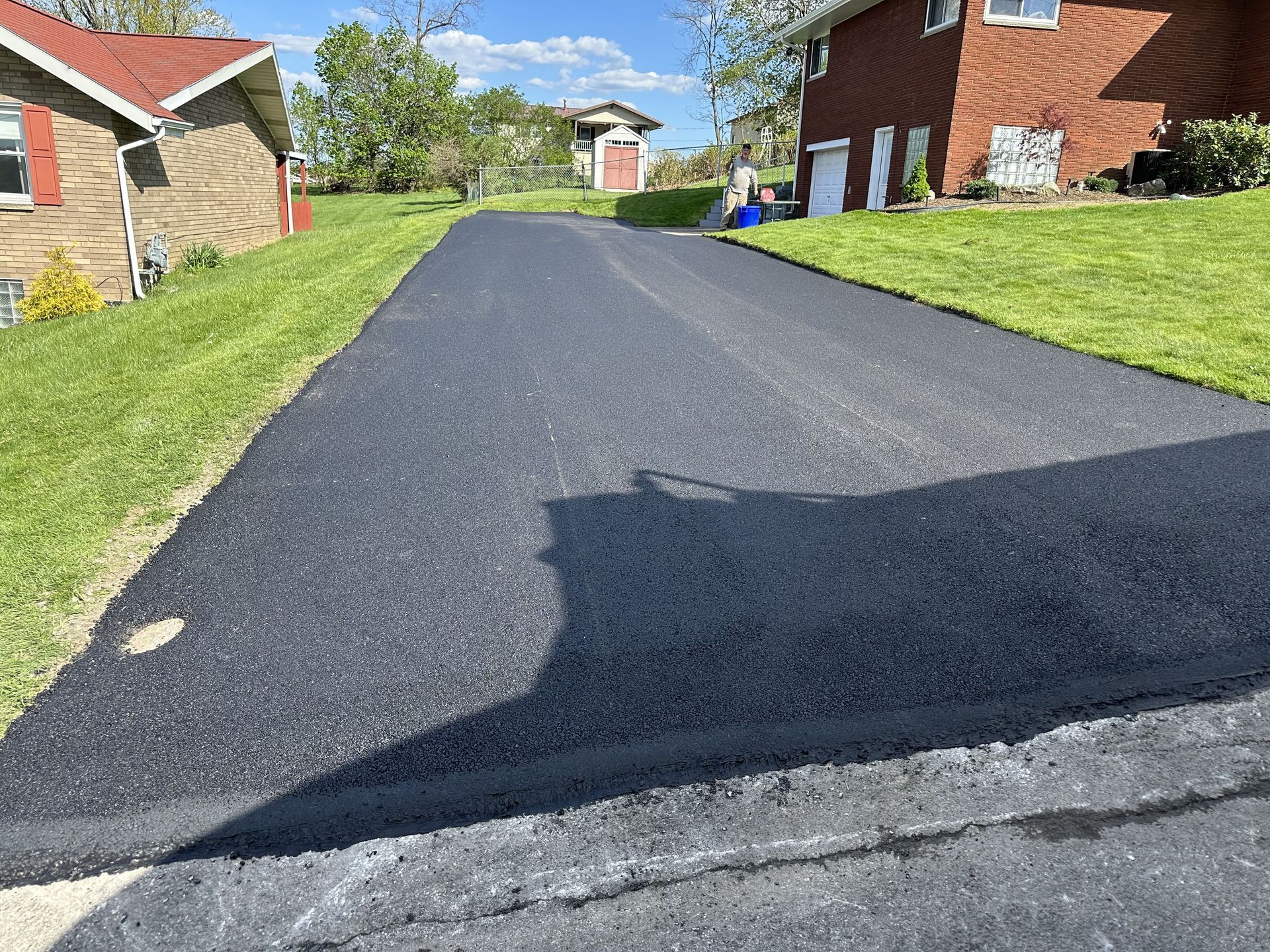 Newly paved asphalt driveway with green grass on either side, leading to a street.