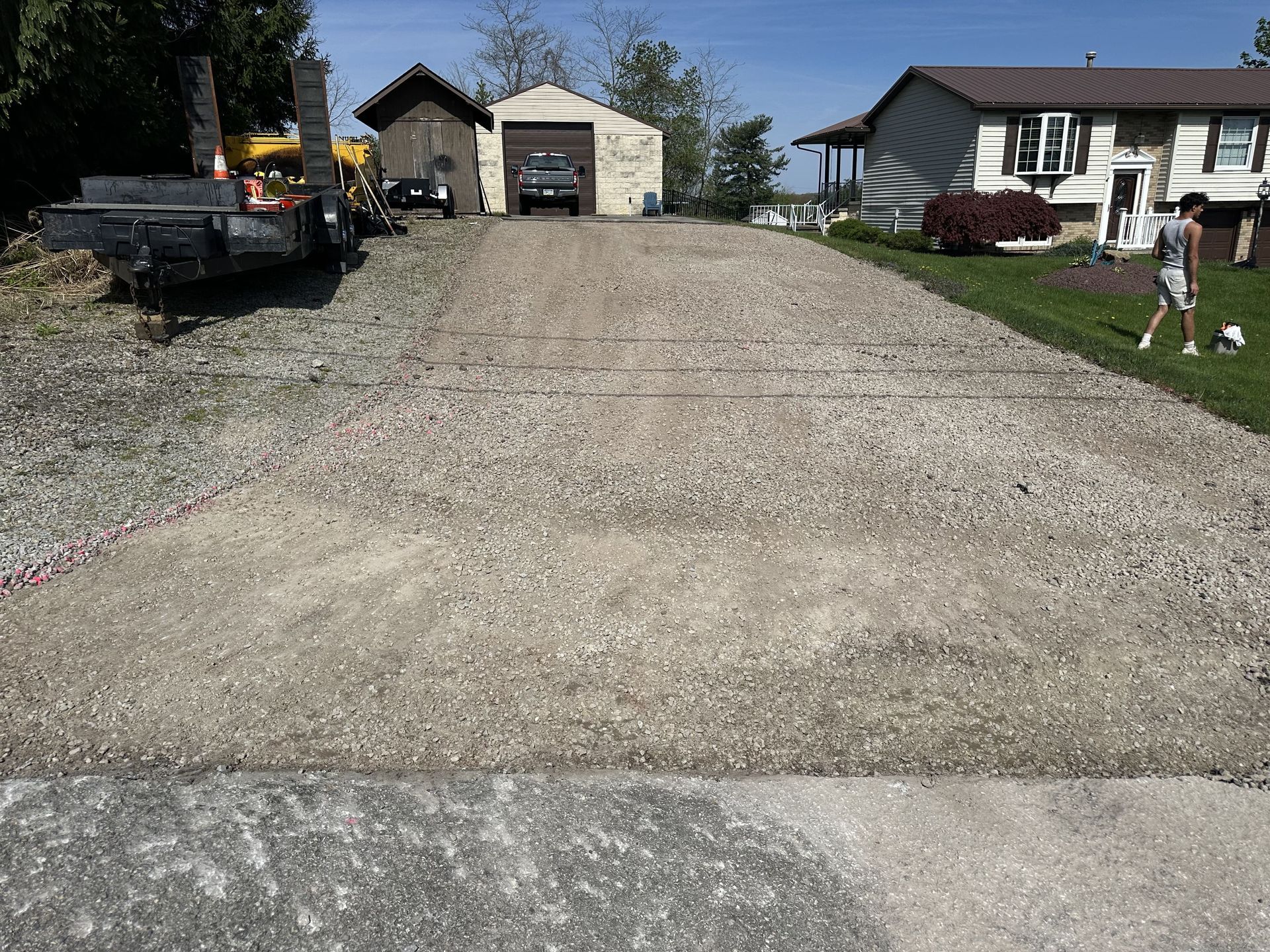 A gravel driveway leading up to a garage, with a house and person visible in the background.