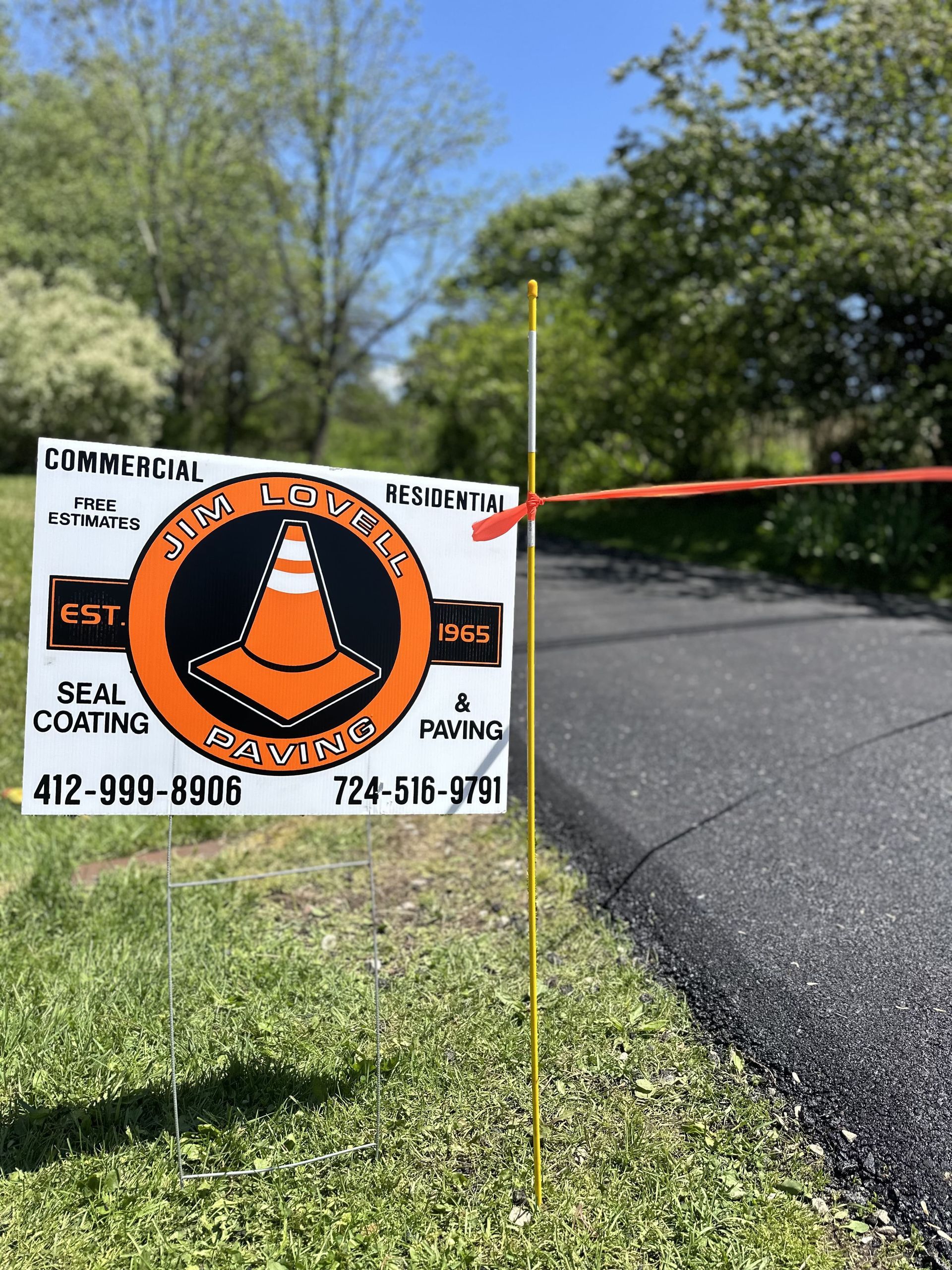 Sign for seal coating and paving with phone numbers on the side of a freshly paved road.