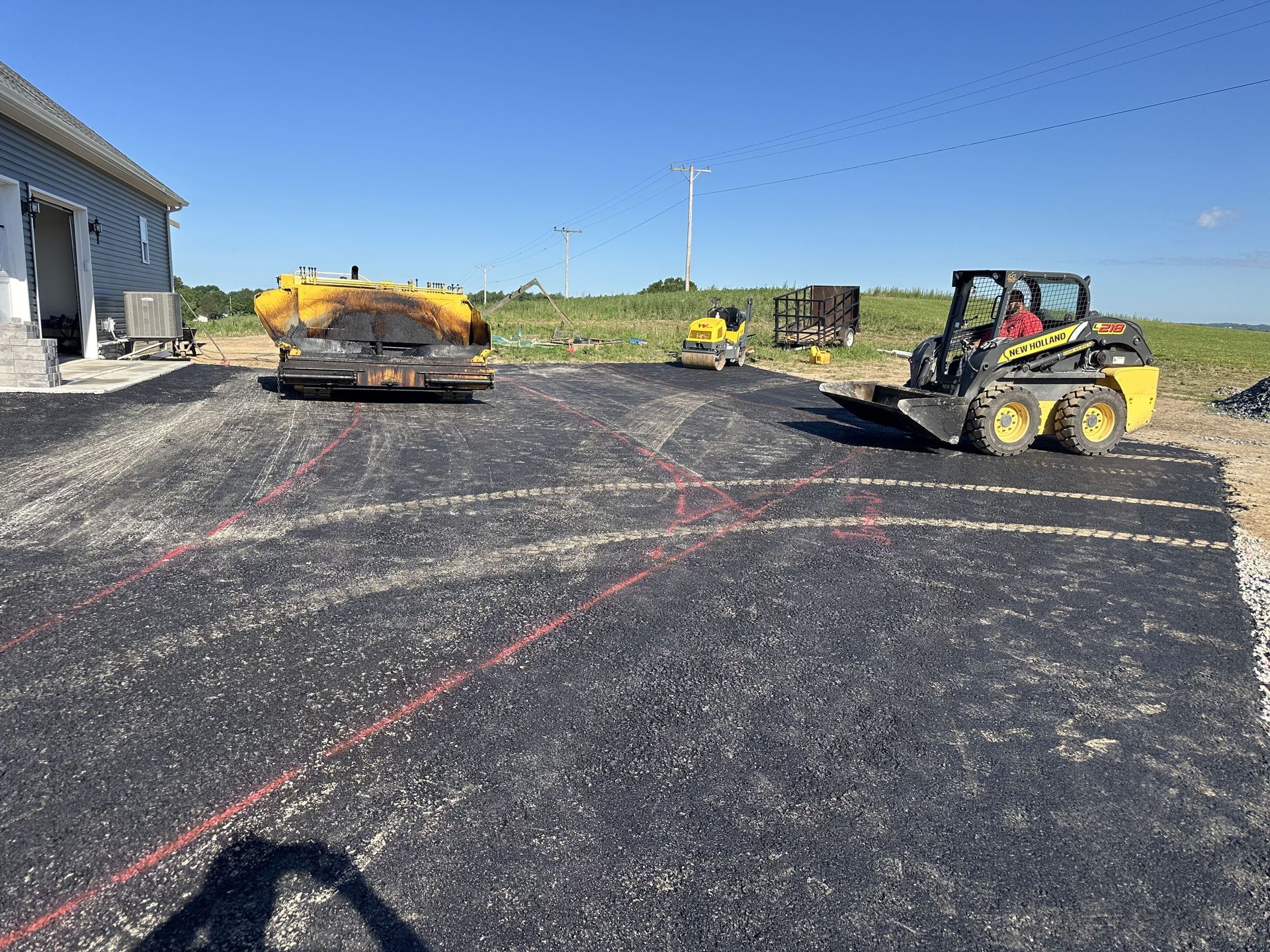 Asphalt paving in progress: Skid steer and machinery compacting fresh asphalt on a parking area.