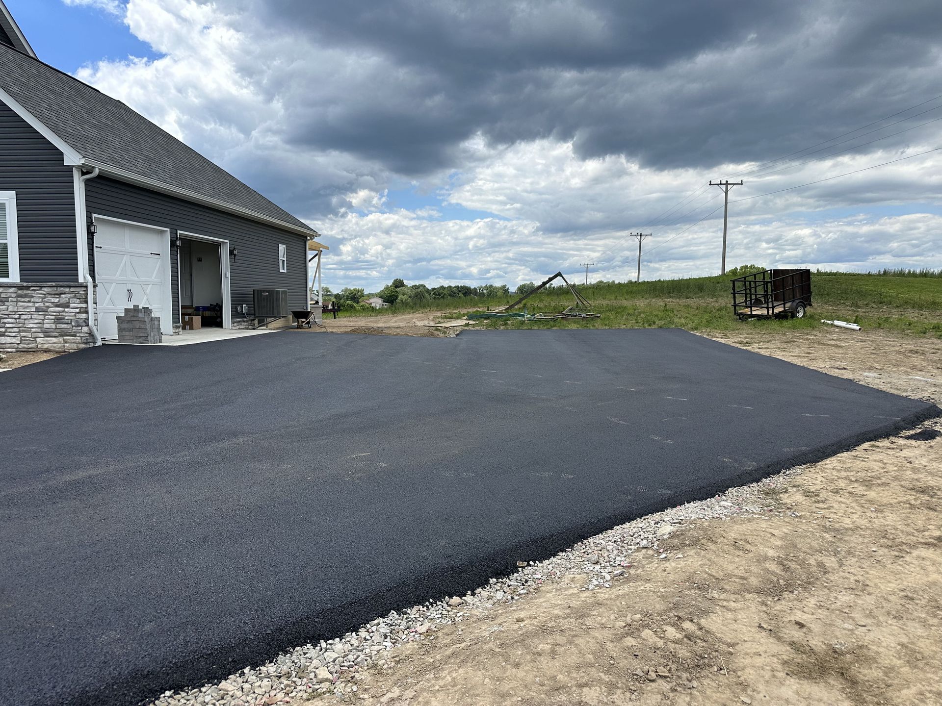 Newly paved asphalt driveway next to a building with a gray facade, under a cloudy sky.