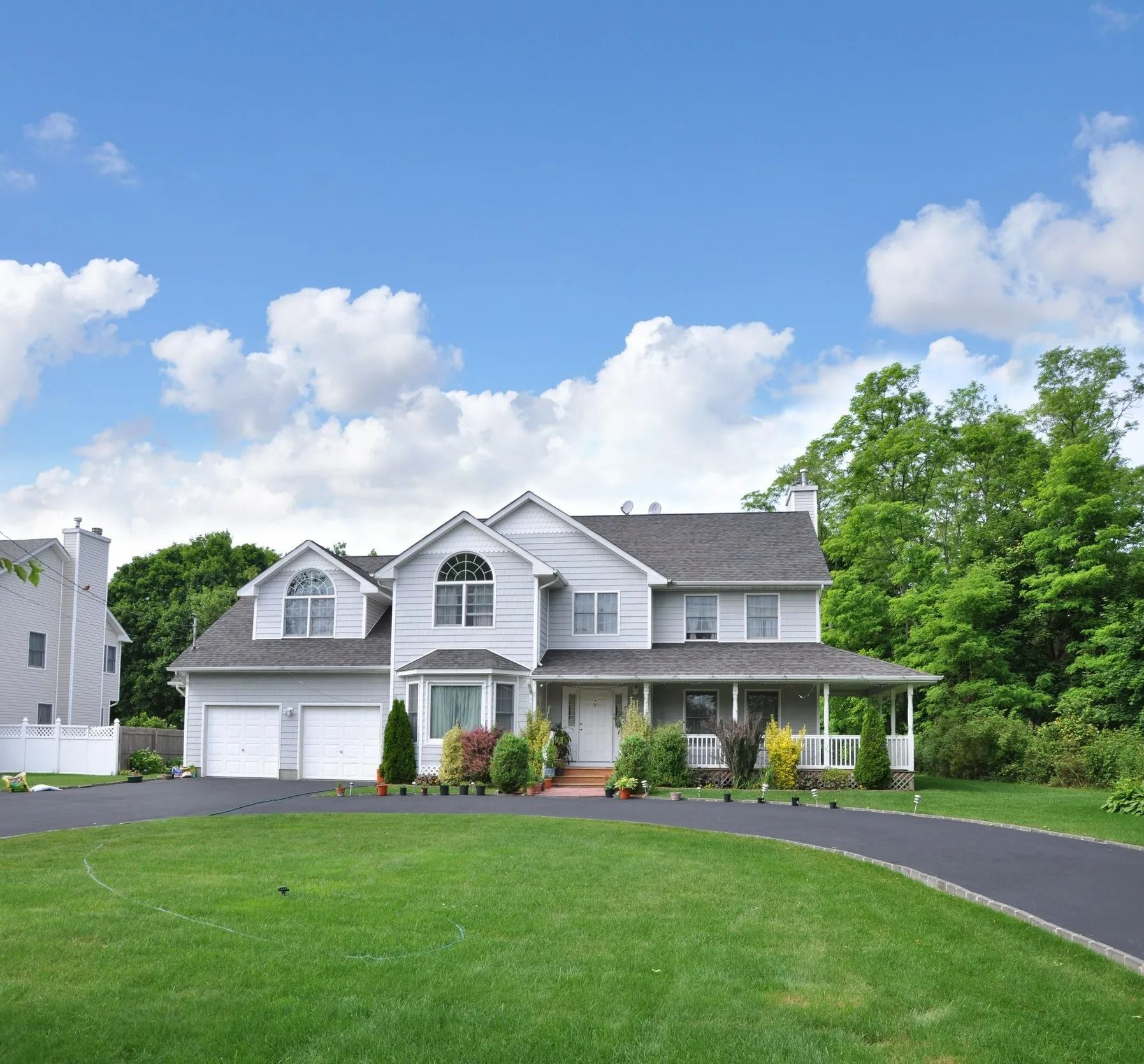 Two-story gray house with green lawn and driveway under a blue sky with white clouds.