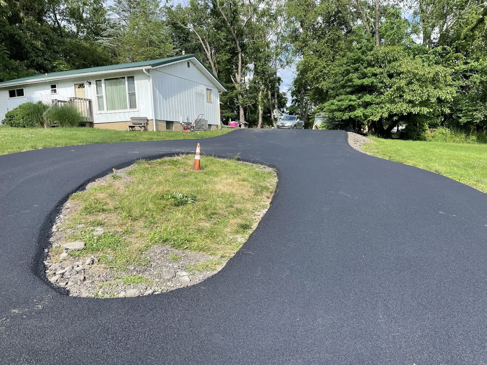 Black asphalt driveway curves to a white house; a grassy island in the middle.