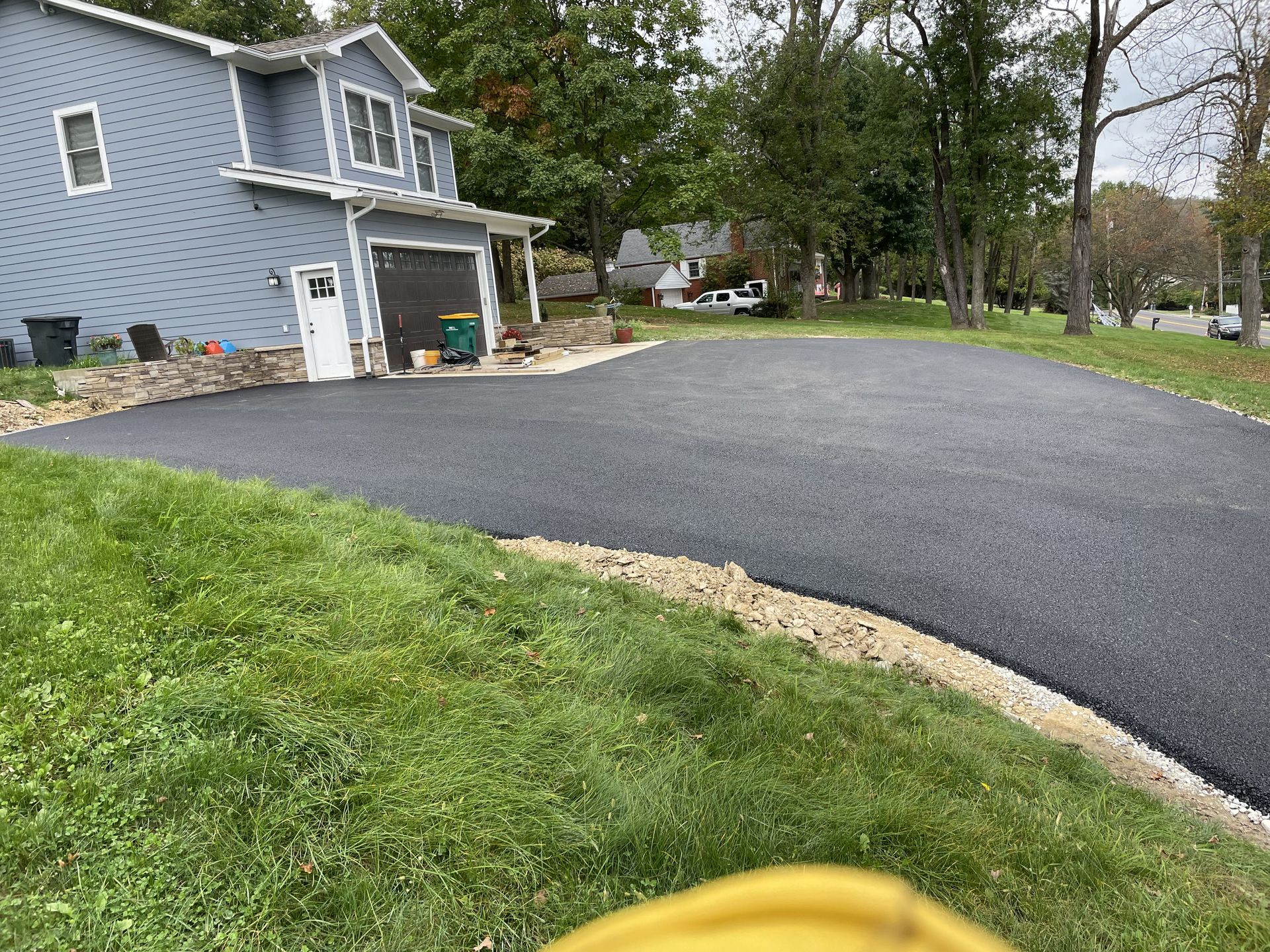 Newly paved asphalt driveway in front of a blue two-story house, bordered by green grass.