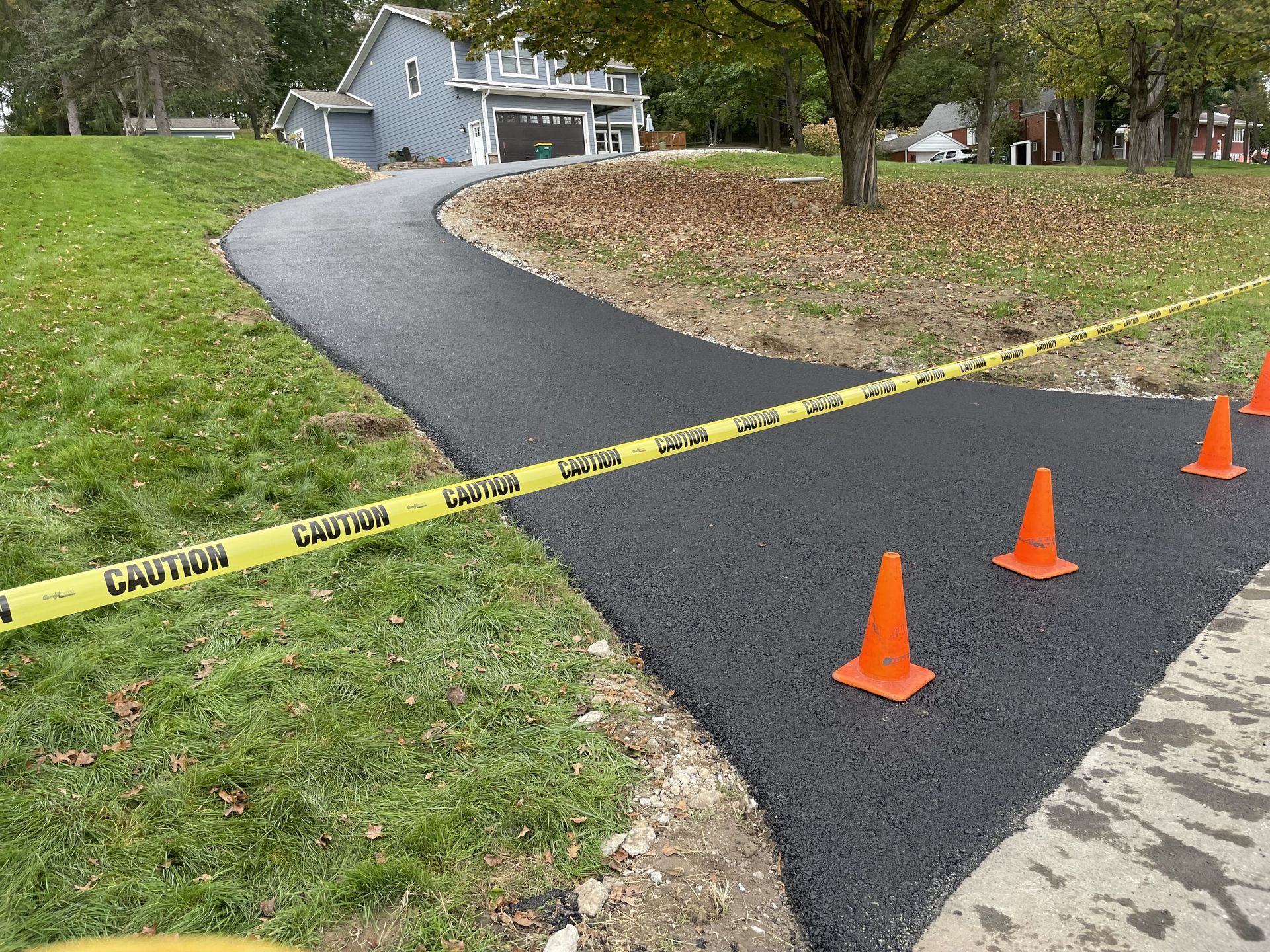New asphalt pathway with caution tape and orange cones in a grassy area.