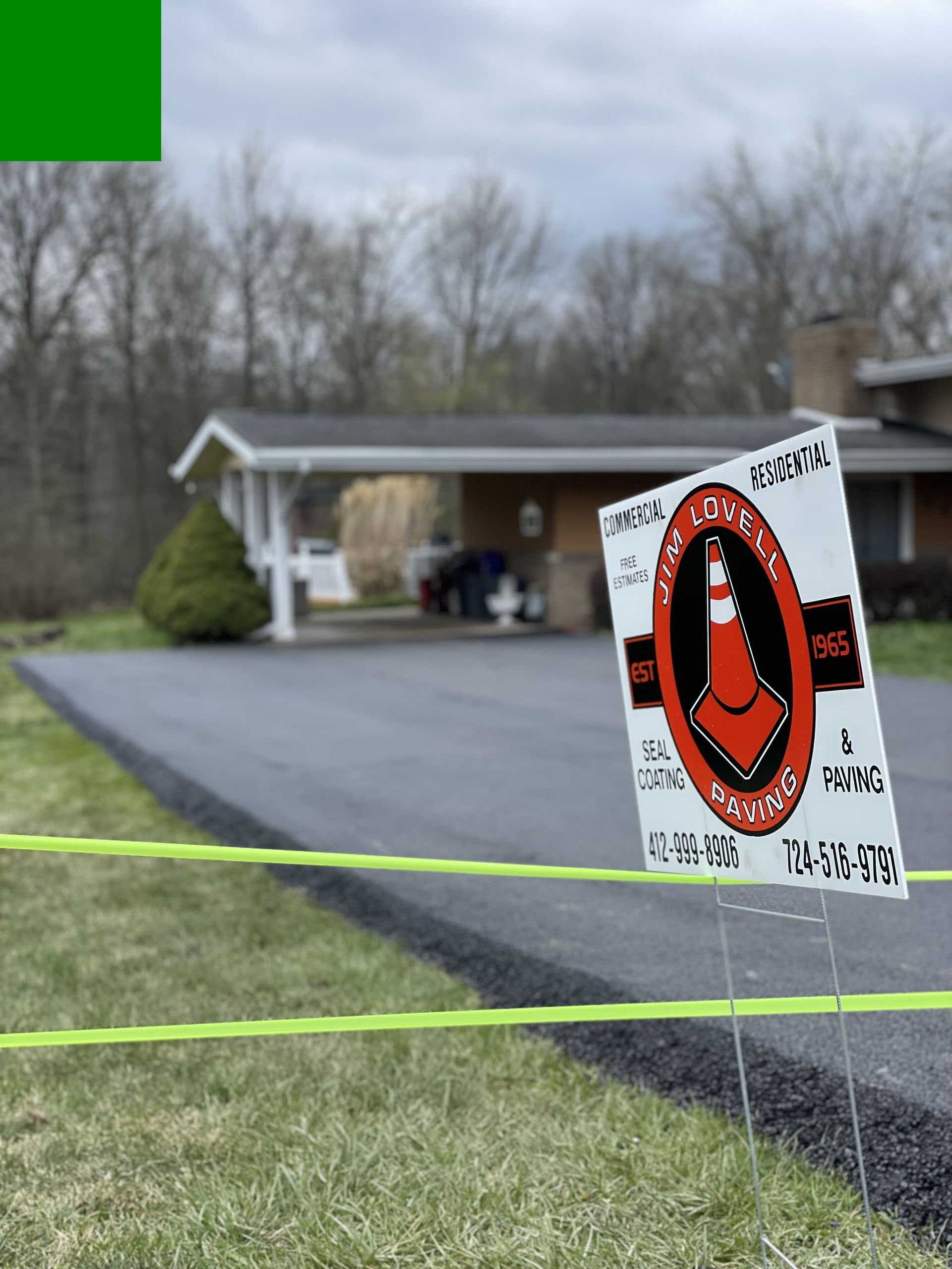 Sign with a traffic cone logo in front of a house, driveway under construction.