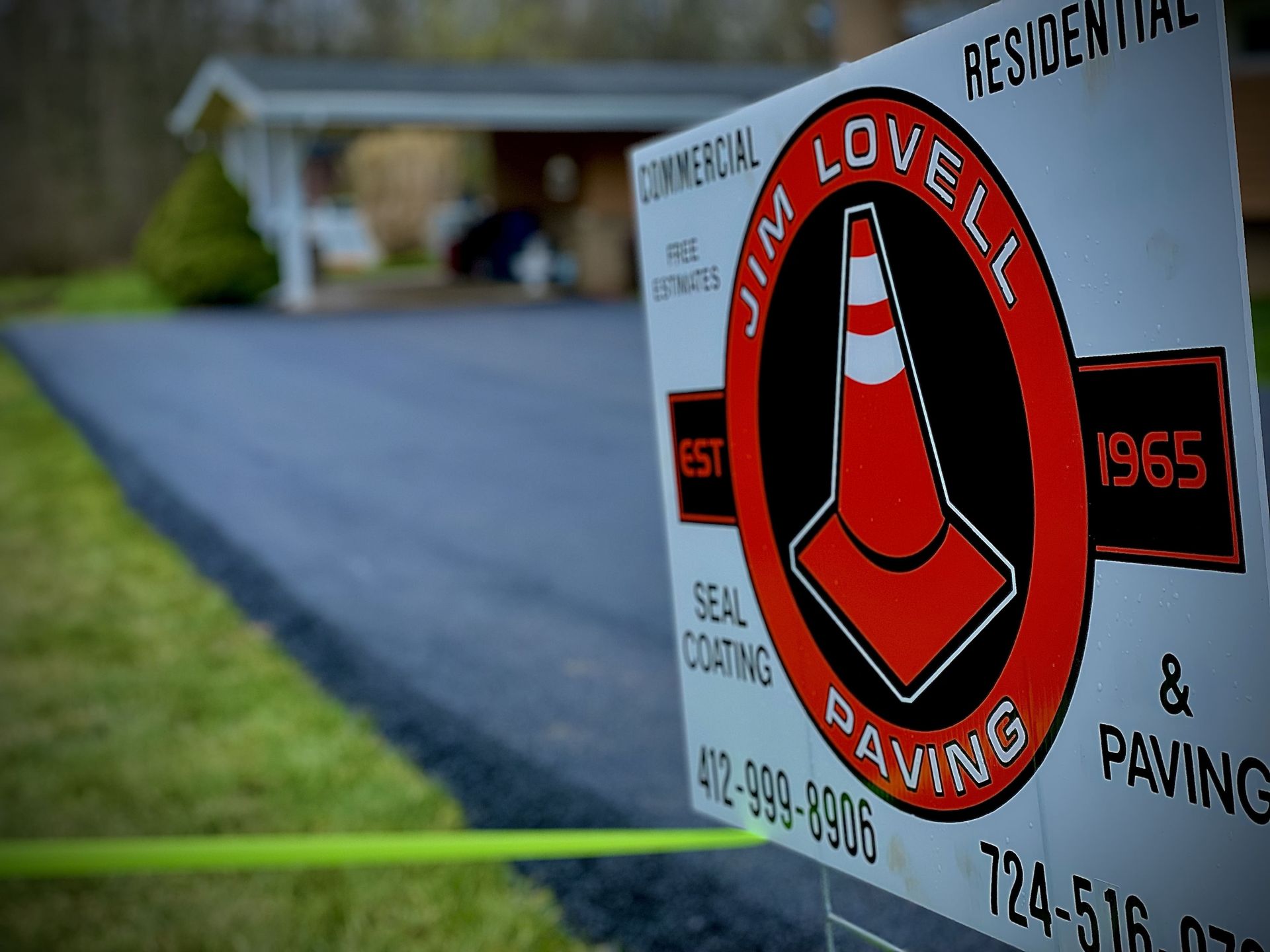 Sign for Jim Lovell Paving with a traffic cone logo, in front of a freshly paved driveway.