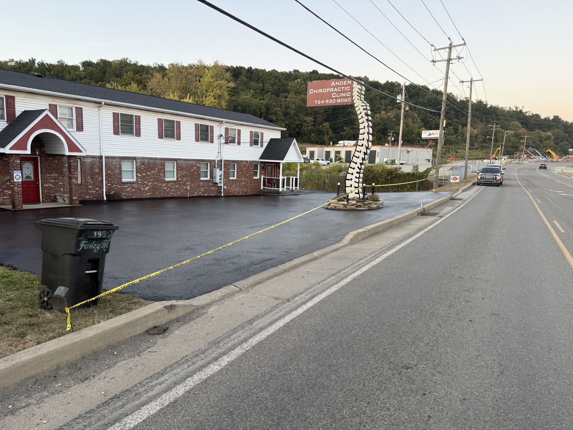 Motel next to a highway. A black trash can and a sign on the property. Yellow tape strung across the ground.