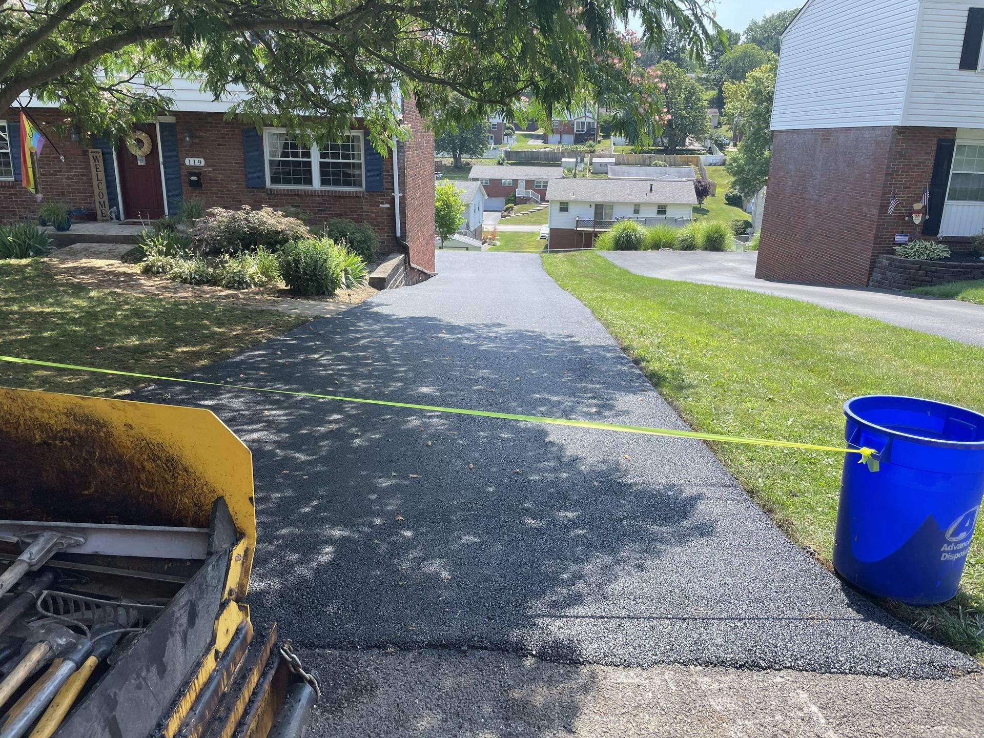 Freshly paved driveway with a machine and a bucket on the side.