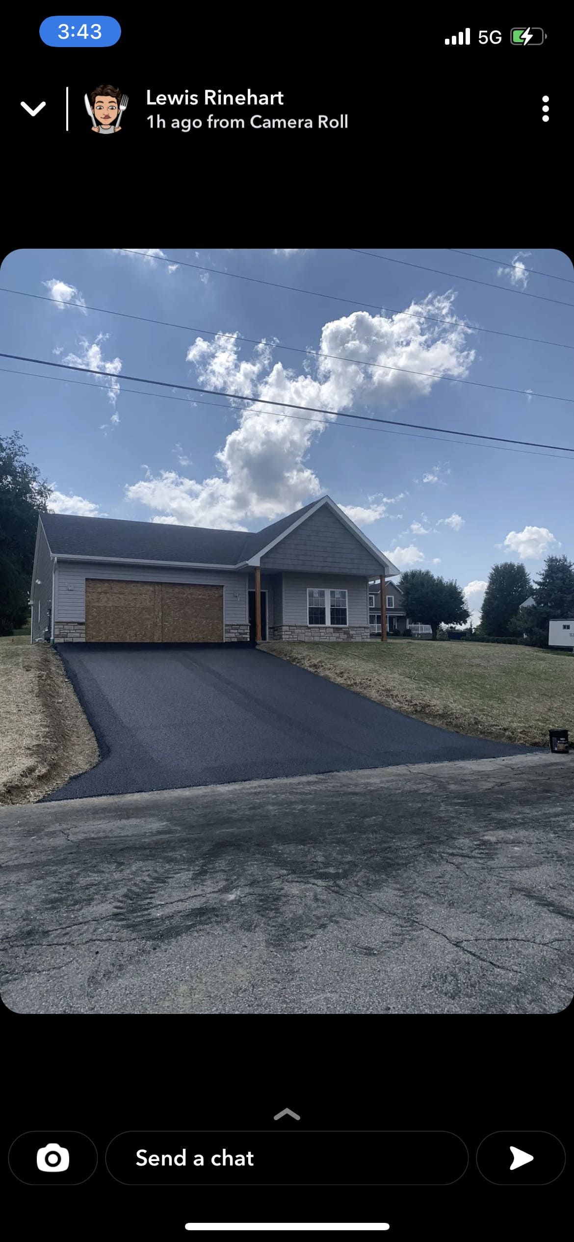 A house with a black driveway under a blue sky, garage doors and a small lawn.