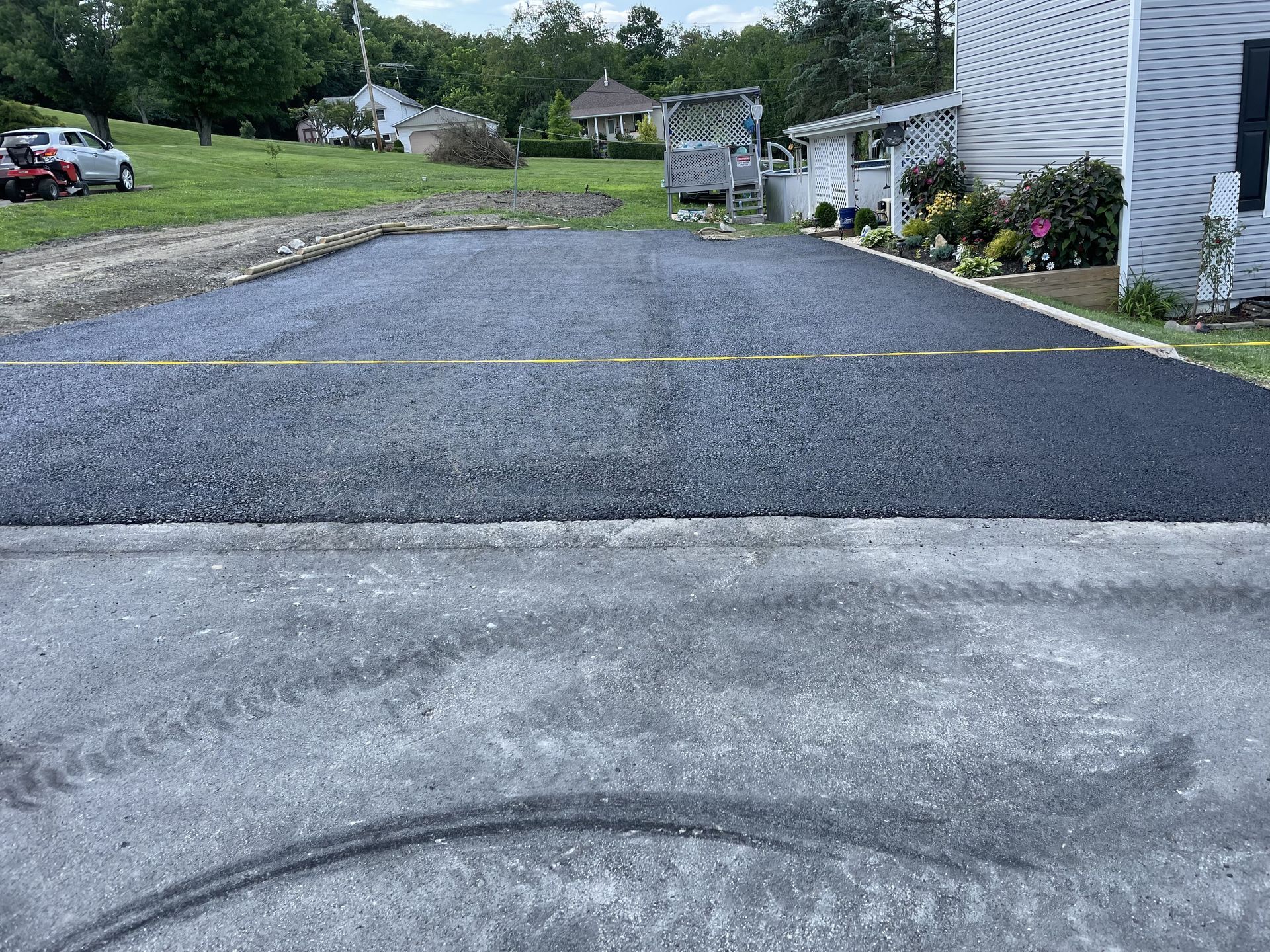 Newly paved asphalt driveway extending towards a house, next to a grassy lawn.