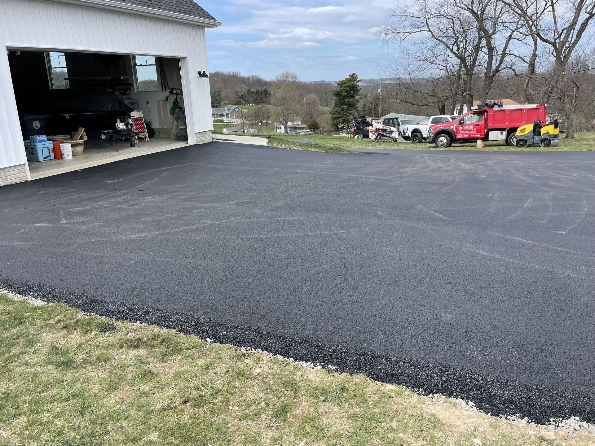 Newly paved asphalt driveway in front of a white garage. A red truck and other vehicles parked nearby.