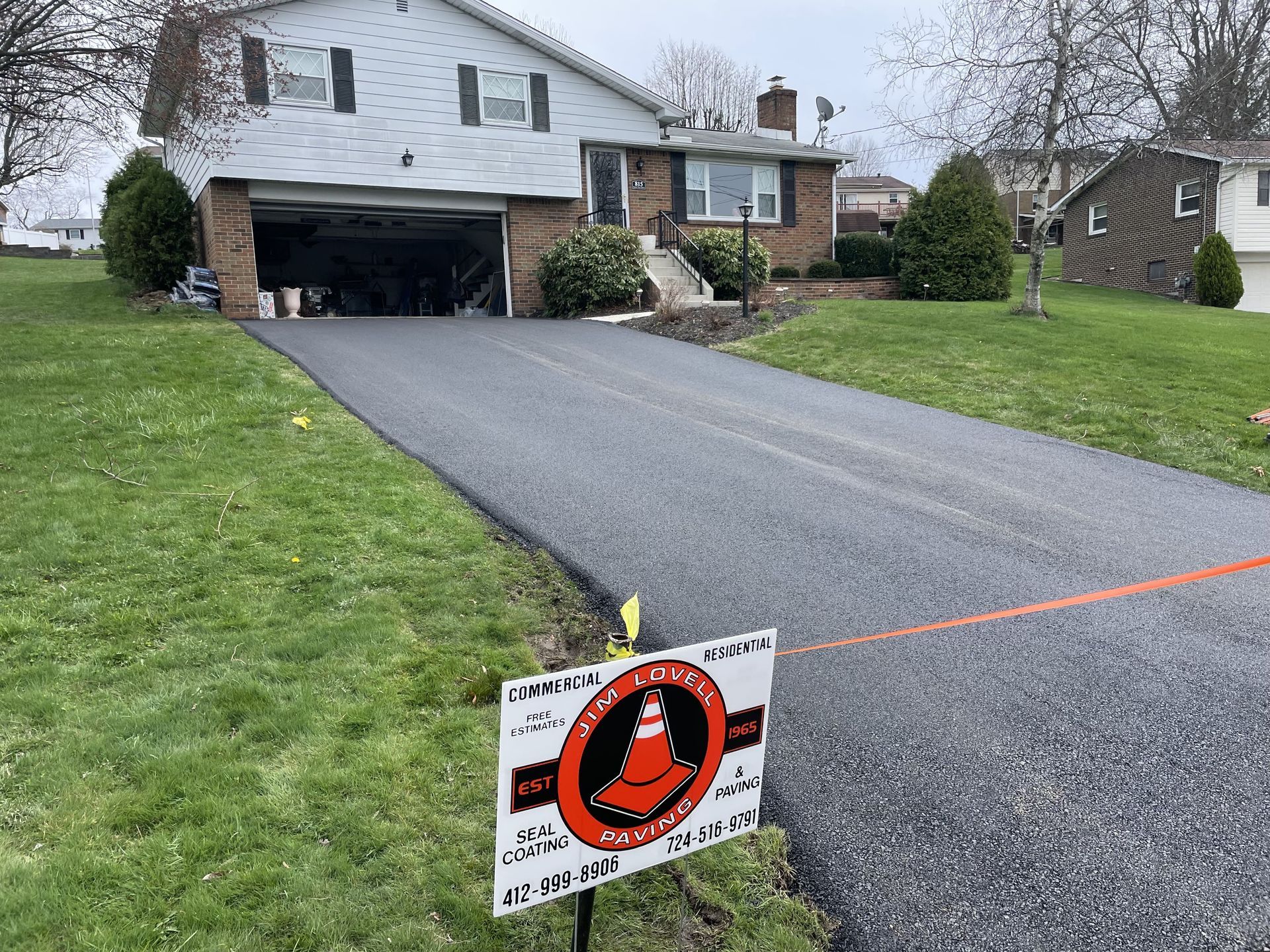 Newly paved asphalt driveway leading to a suburban house with a garage door open.