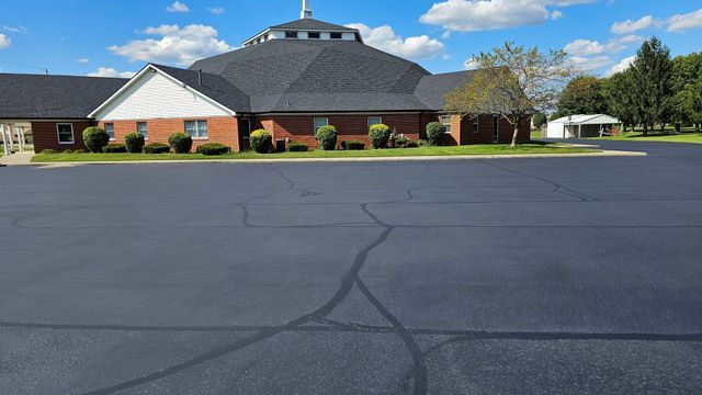 Brick building with a gray roof behind an empty asphalt parking lot on a sunny day