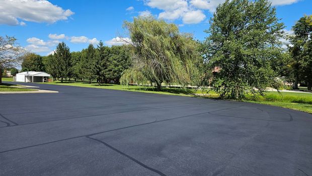 Paved parking lot beside green trees under a bright blue sky with scattered clouds