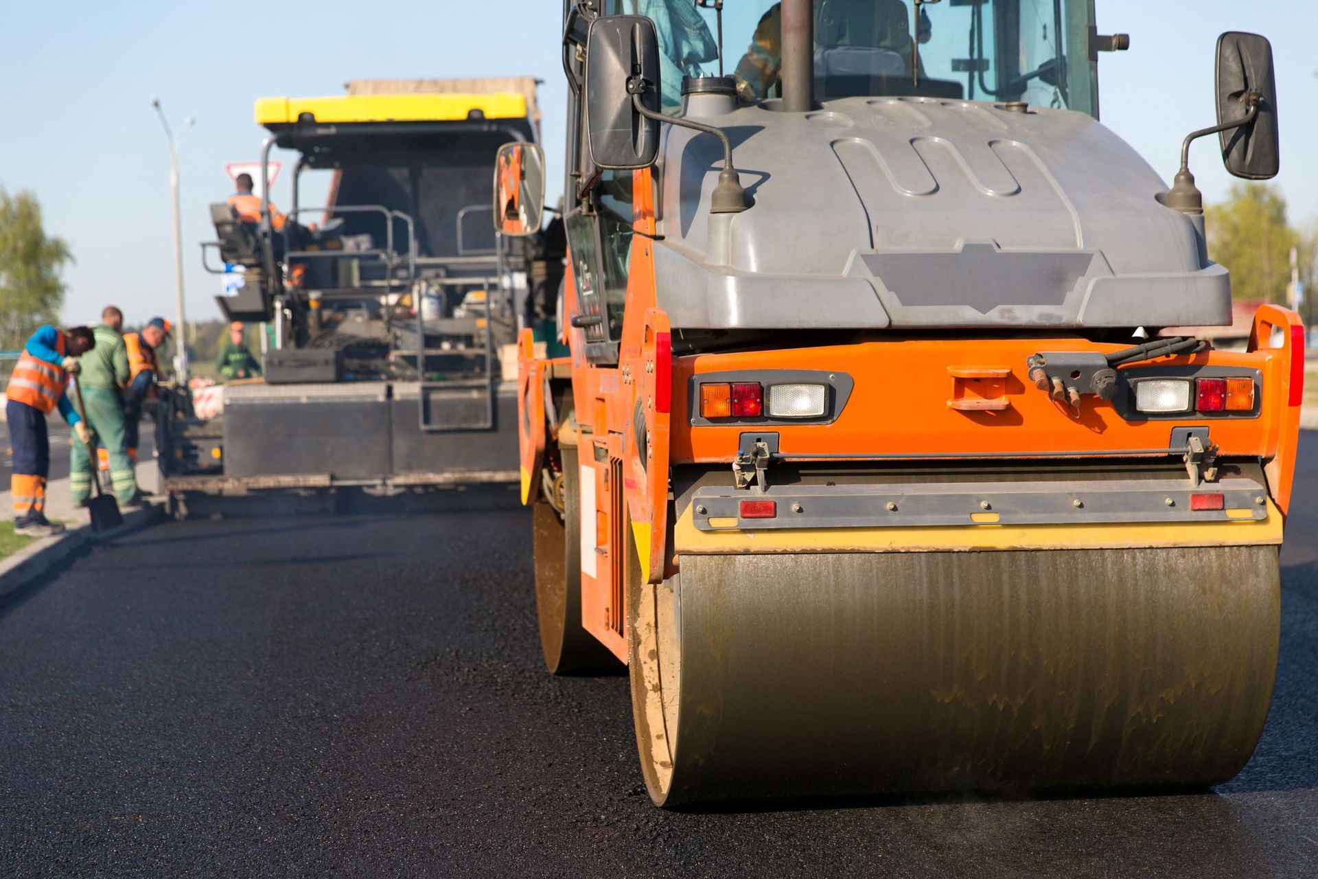 Road paving crew using orange road roller and asphalt paver on a highway under construction
