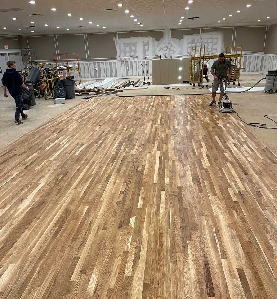 A man is cleaning a large wooden floor with a vacuum cleaner.