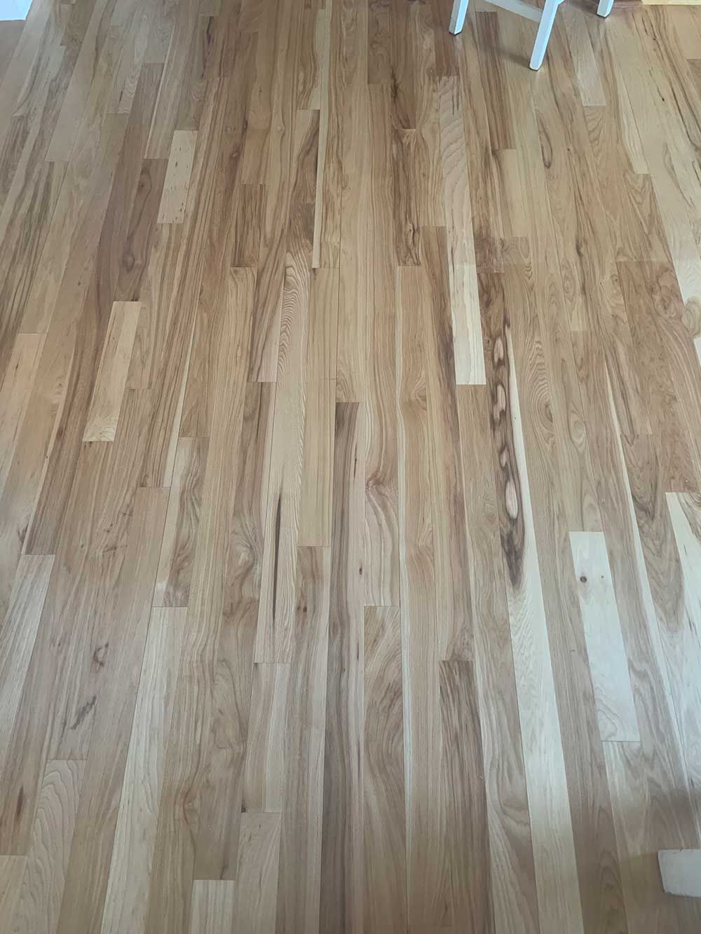A close up of a wooden floor with a chair in the background.
