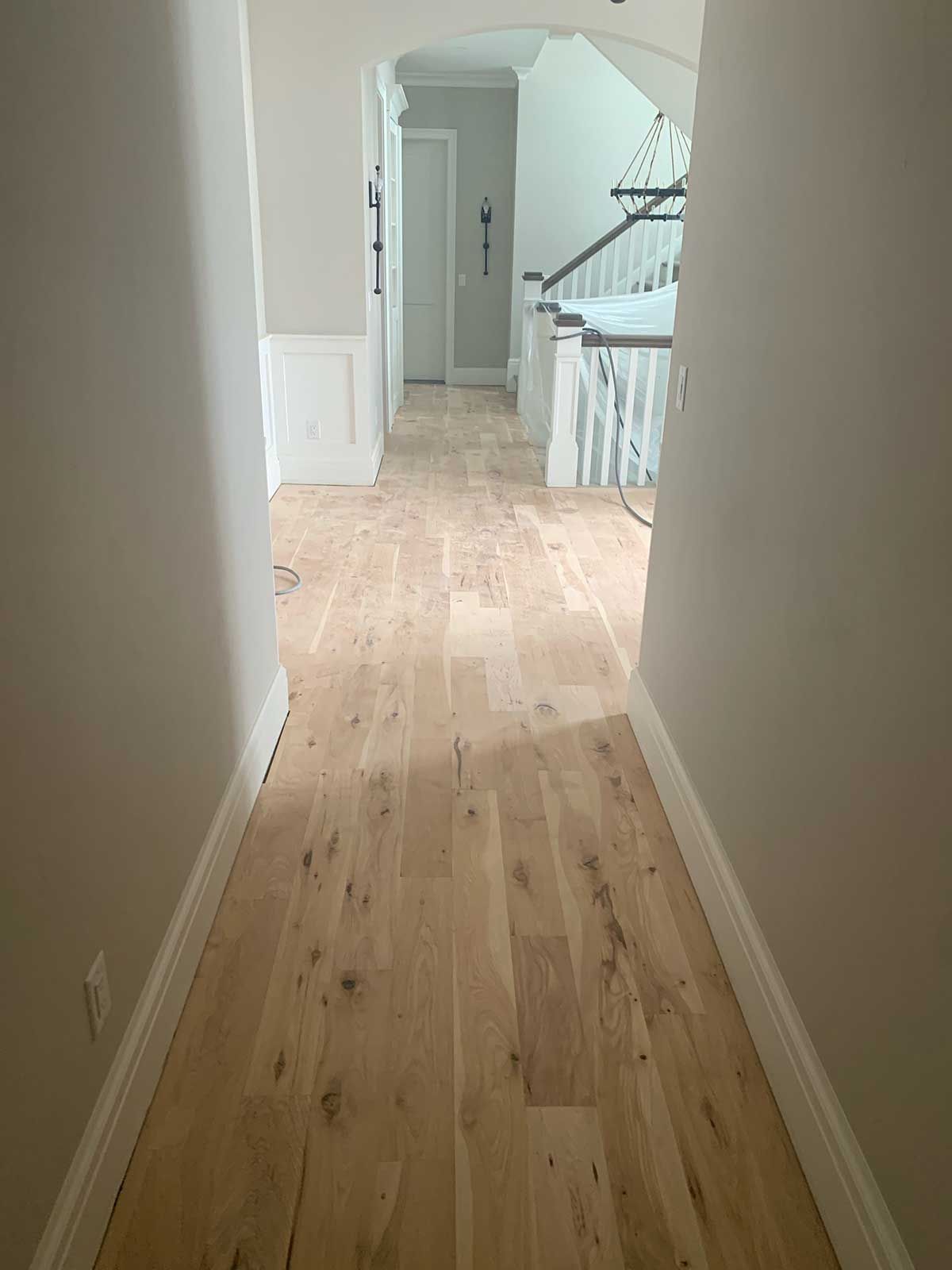 A hallway with hardwood floors and a staircase in the background.