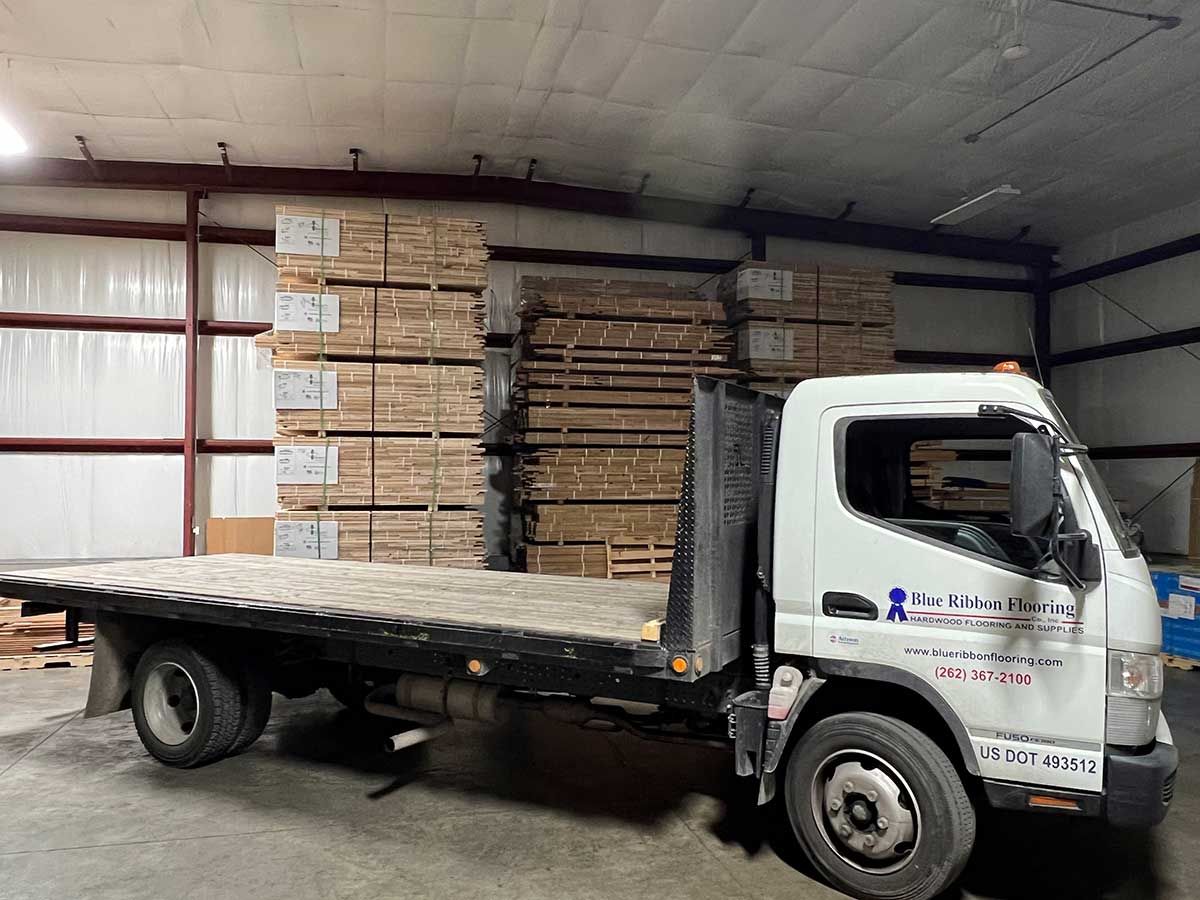 A white truck with a flat bed is parked in a warehouse.