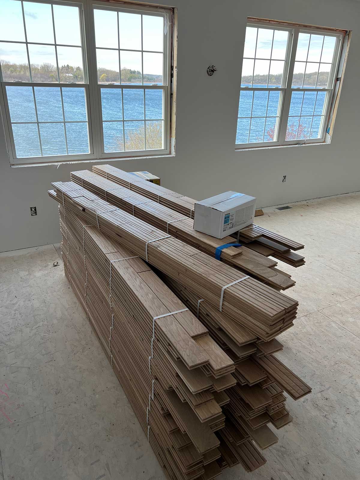 A pile of wood is sitting on the floor in front of two windows