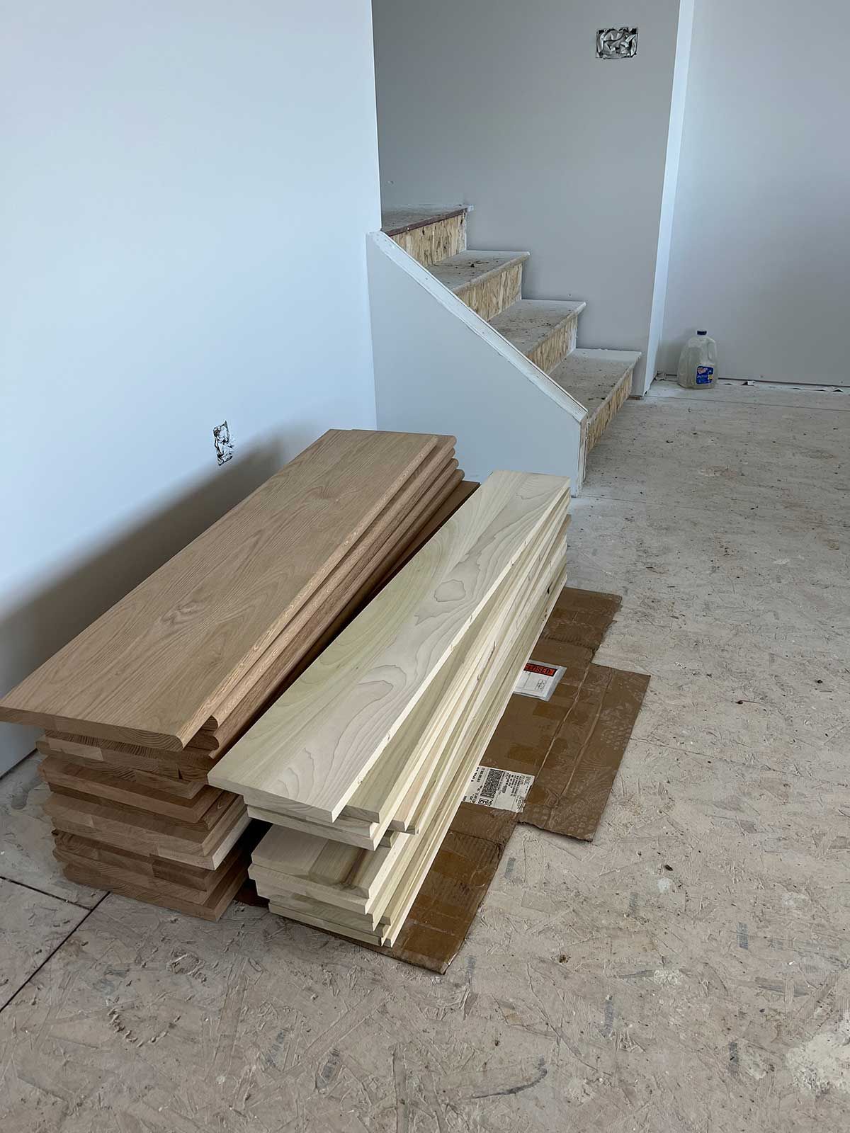 A pile of wood is sitting on the floor next to a staircase.
