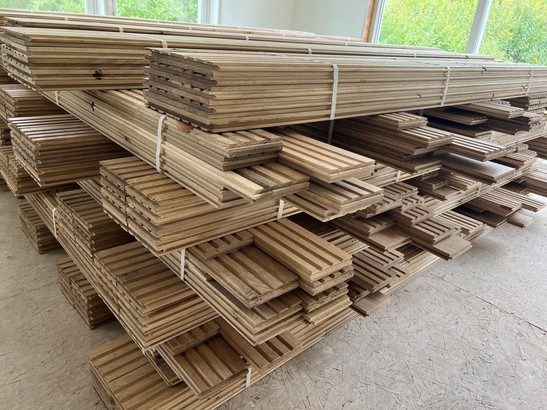 Pile of wooden deck boards, various sizes, stacked indoors.