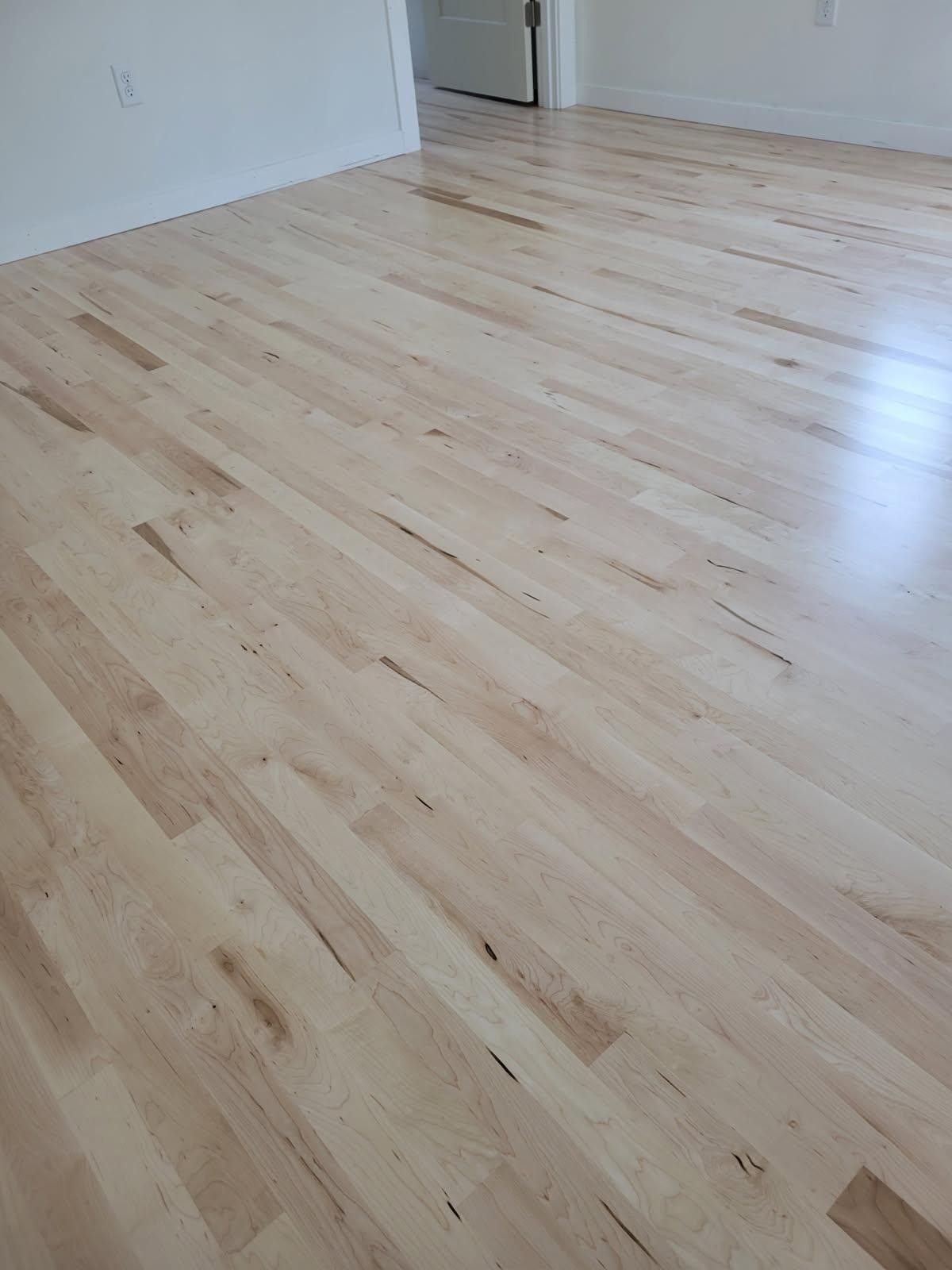 Light-colored hardwood flooring in a room, with visible grain patterns and some dark spots.
