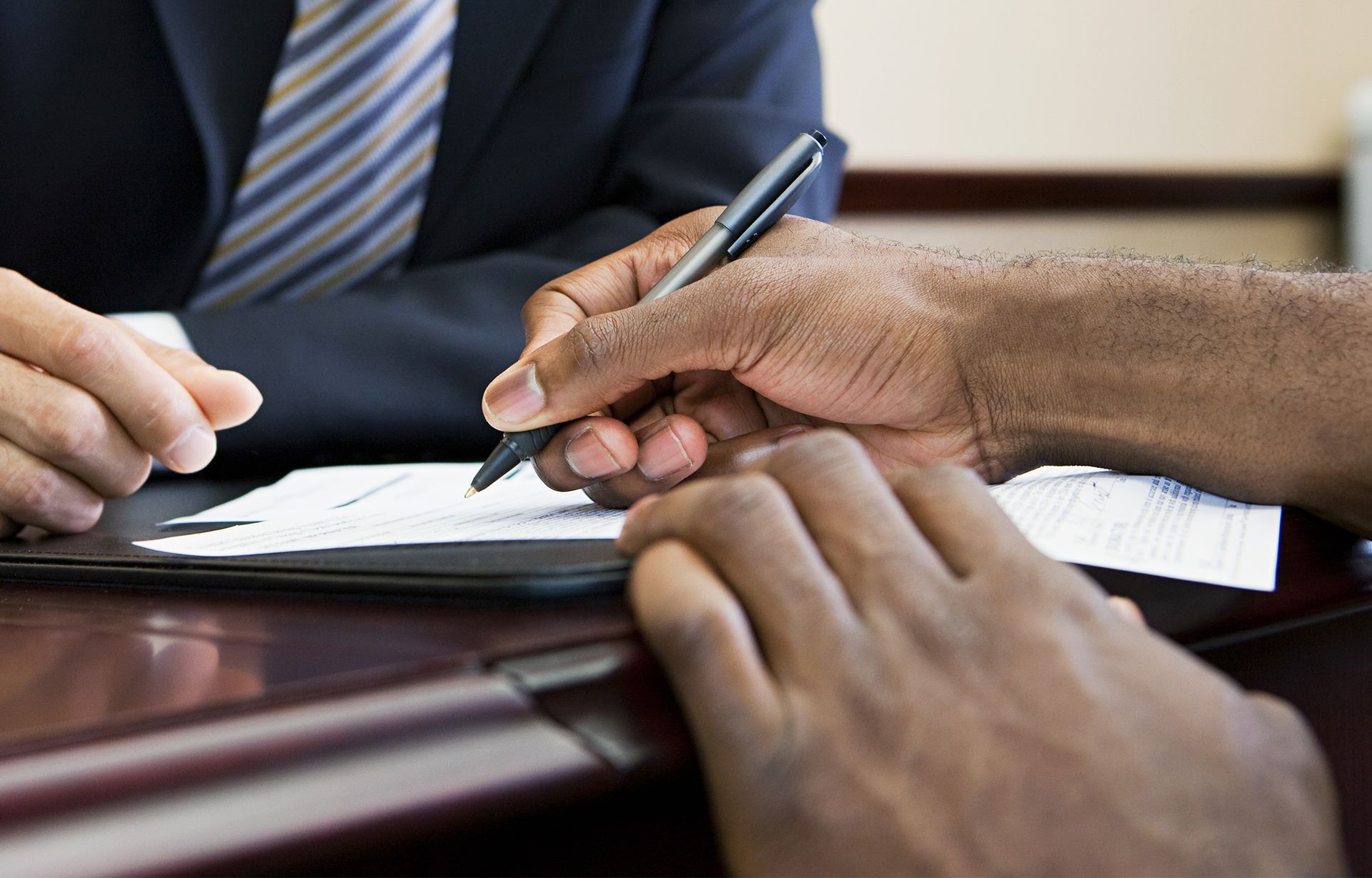 A man in a suit and tie is signing a document with another man.