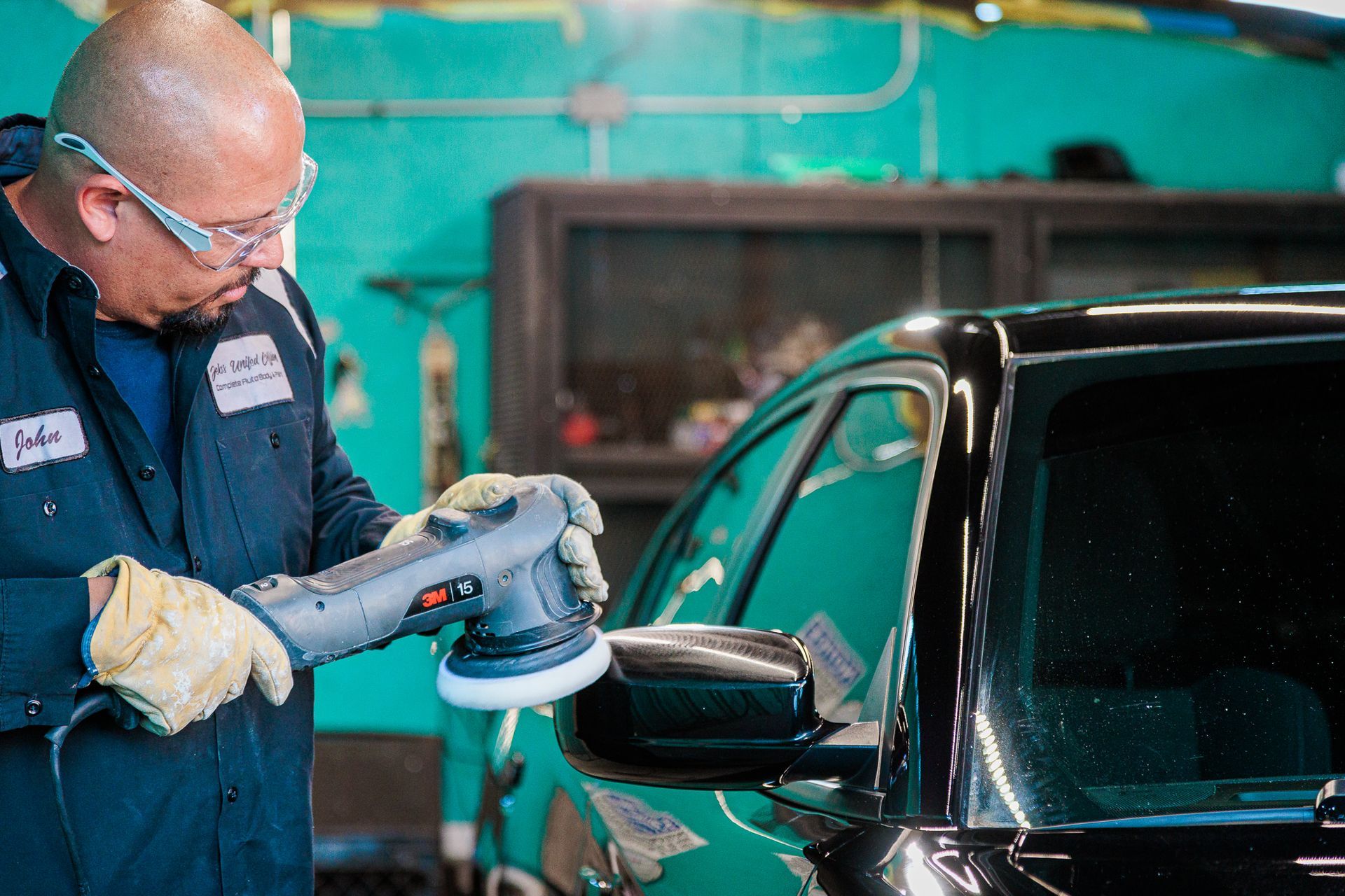 A man is polishing a car with a machine in a garage.