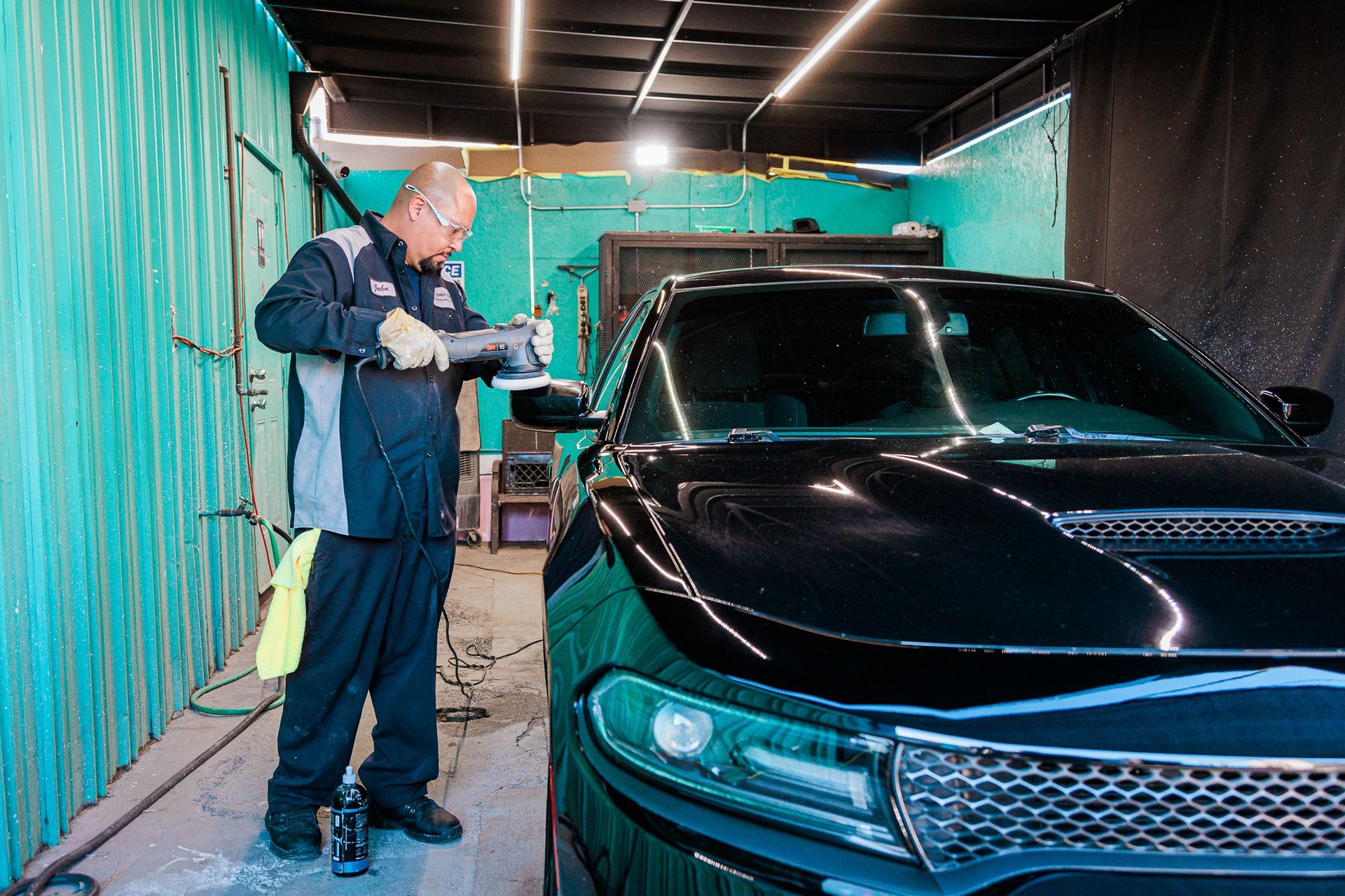 A man is standing next to a black car in a garage.