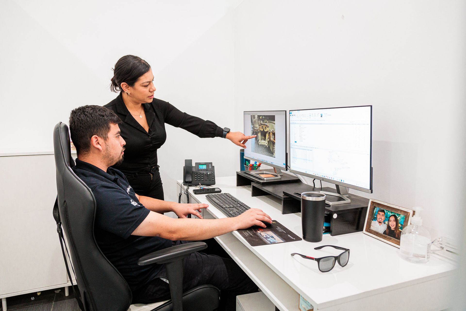 A woman is pointing at a computer screen while a man sits at a desk.
