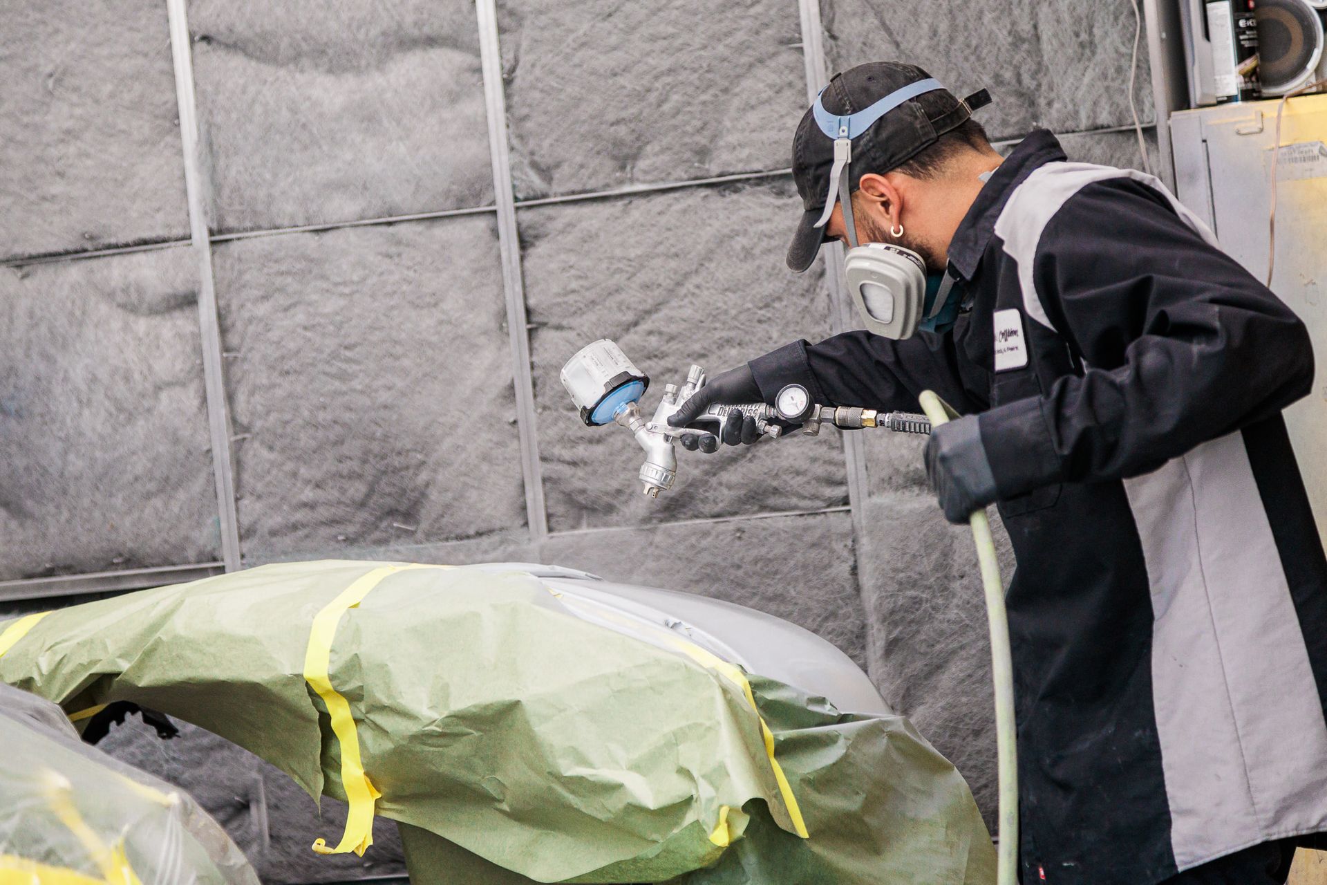 A man wearing a mask is spray painting a car.
