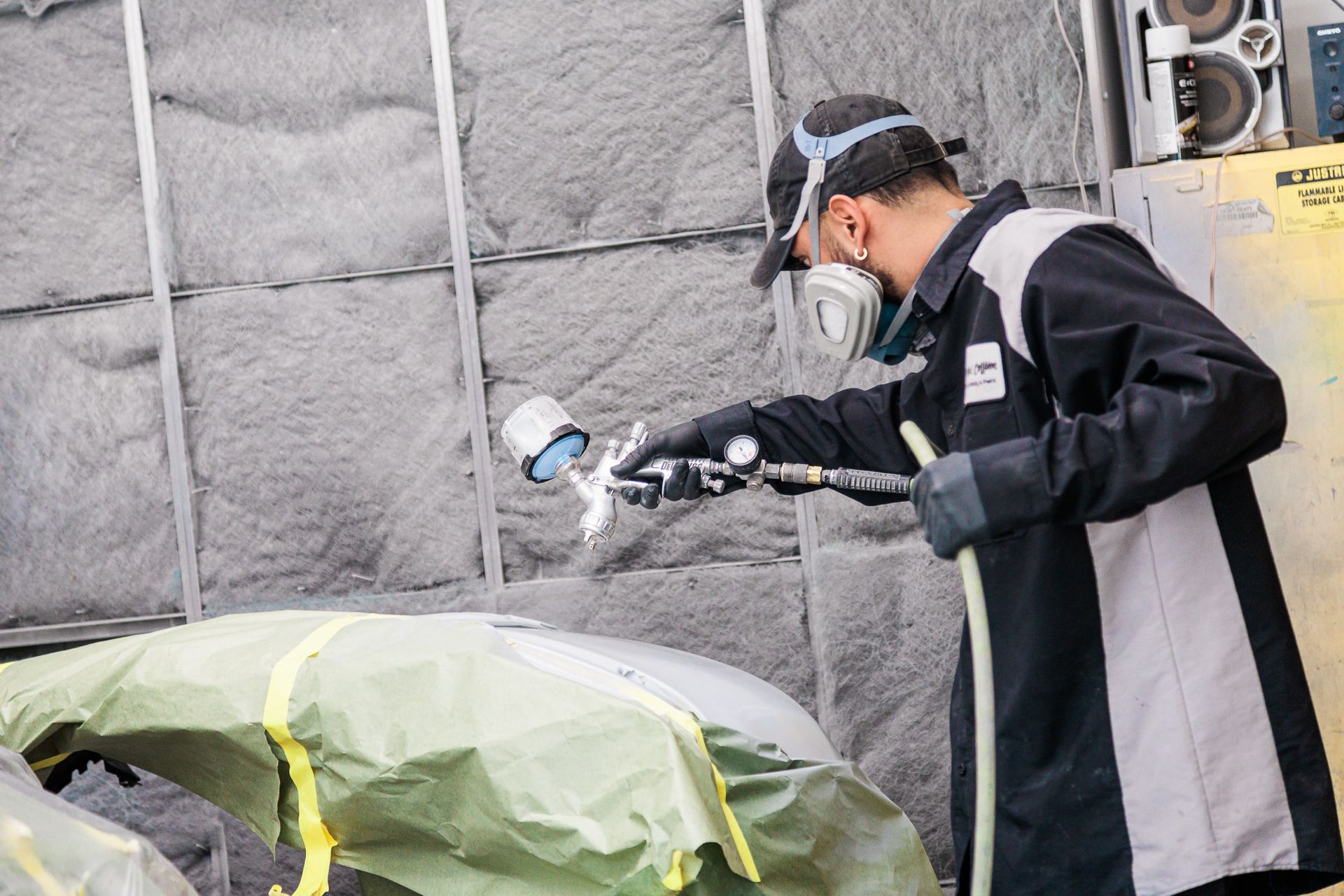 Man wearing a mask is spray painting a car.