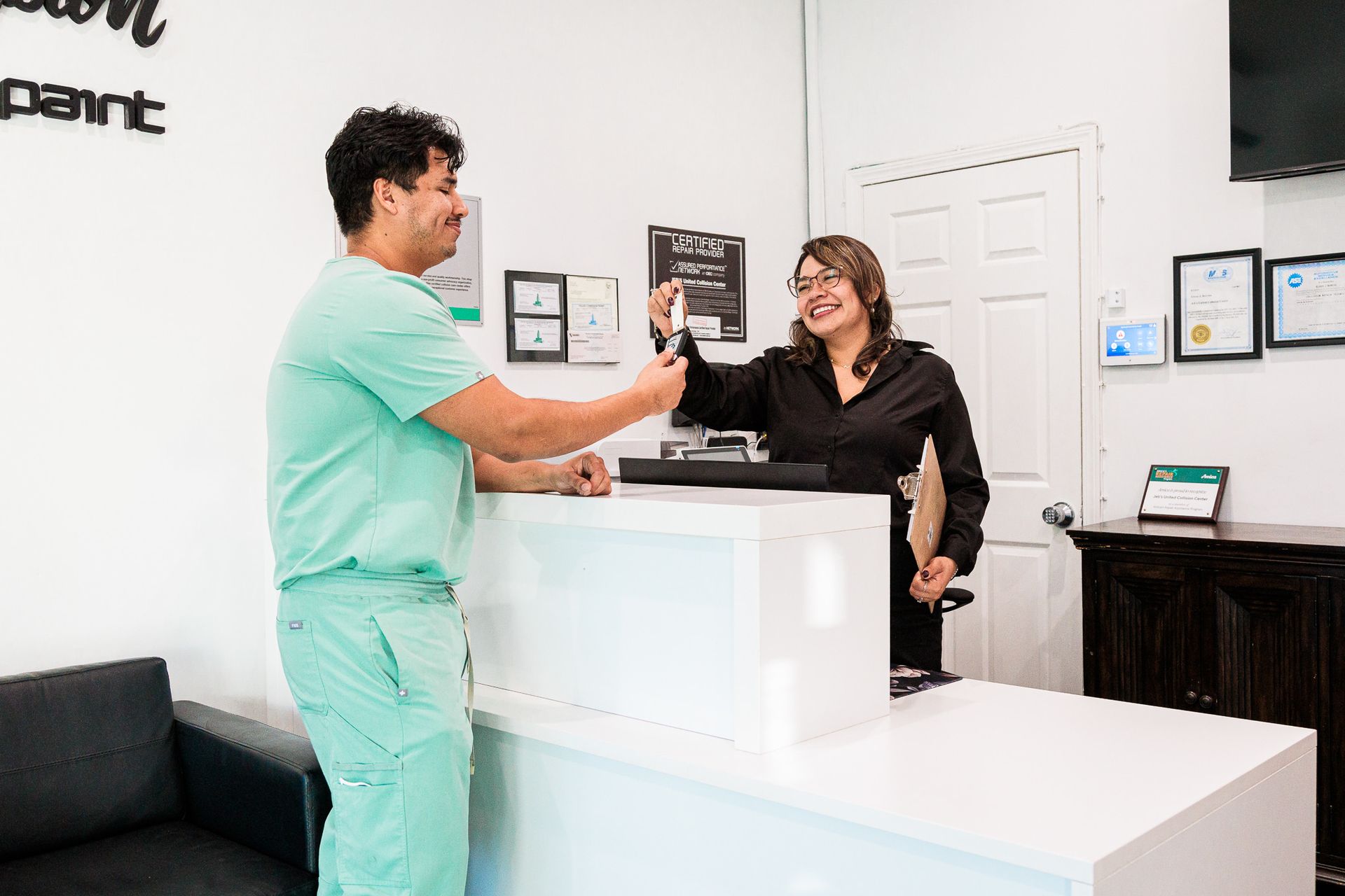 A man and a woman are standing at a counter in a collision repair shop