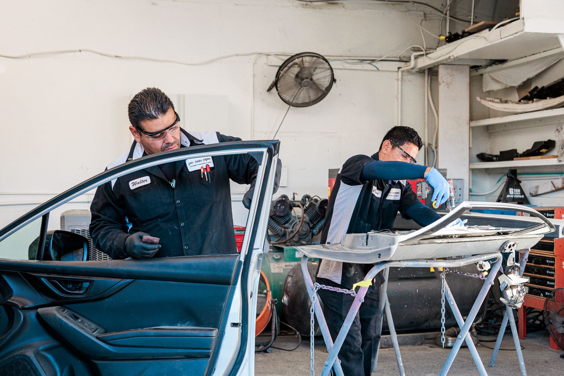 Two men are working on a car windshield in a garage.