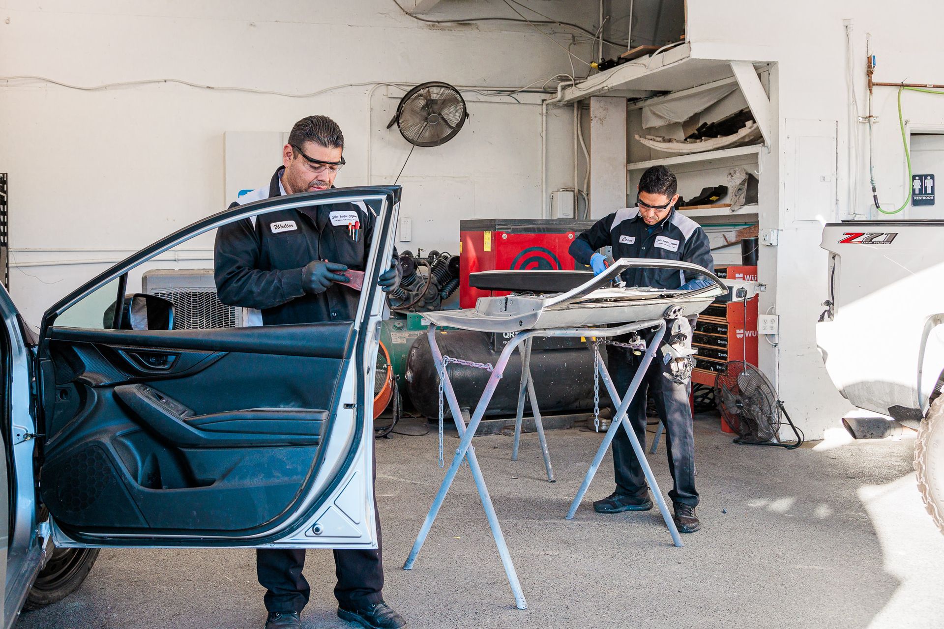 Two men are working on a car in a garage.
