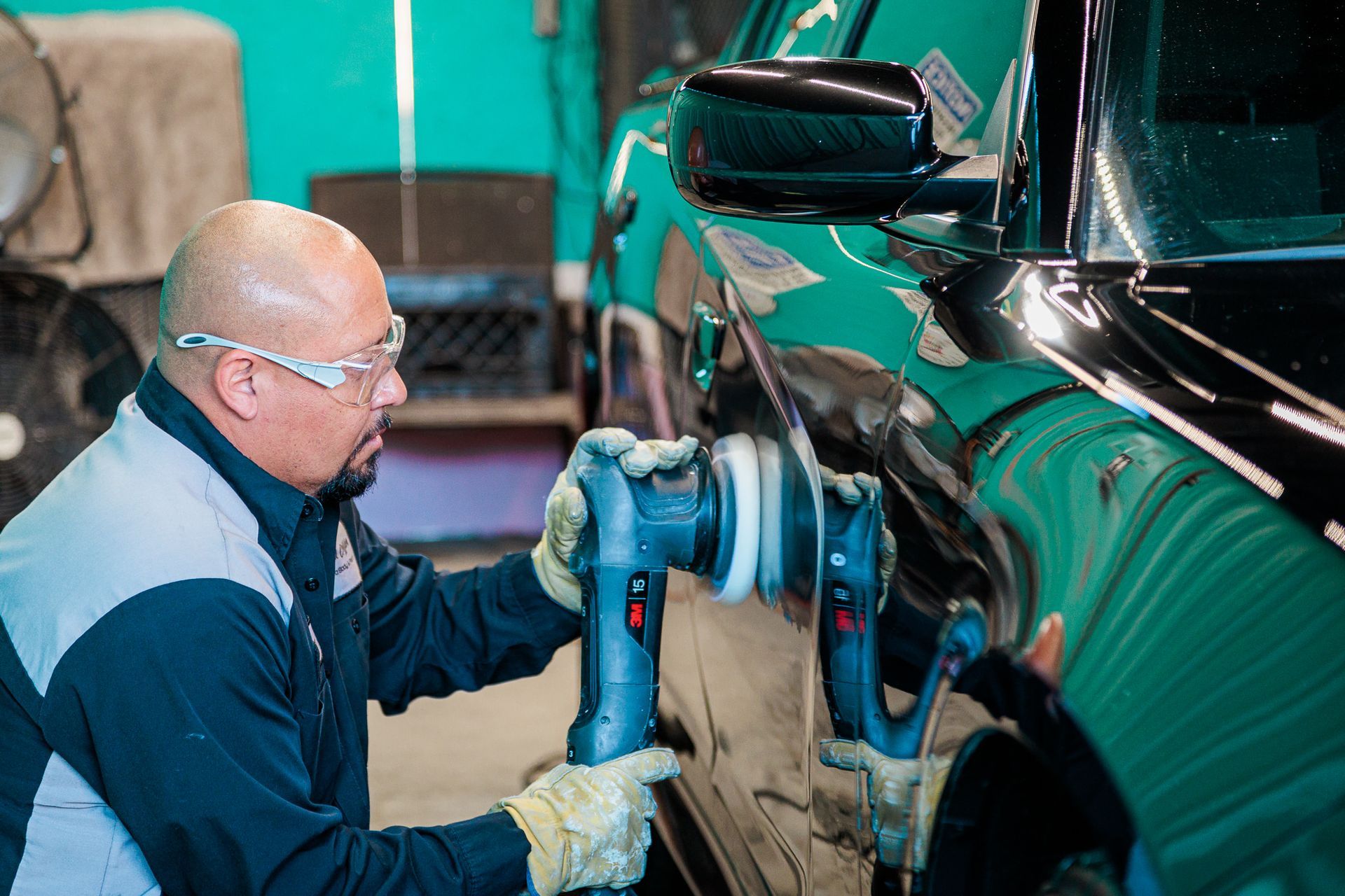A man is polishing a car with a machine in a garage.