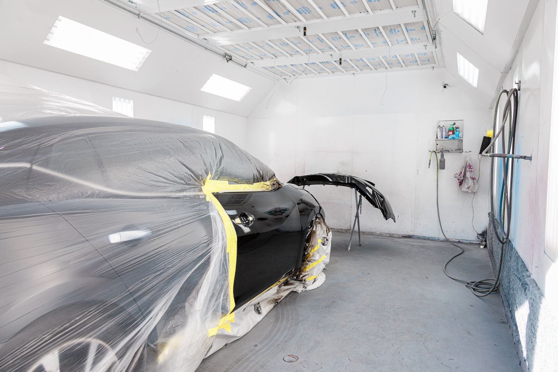 A black car is covered in plastic in a paint booth.