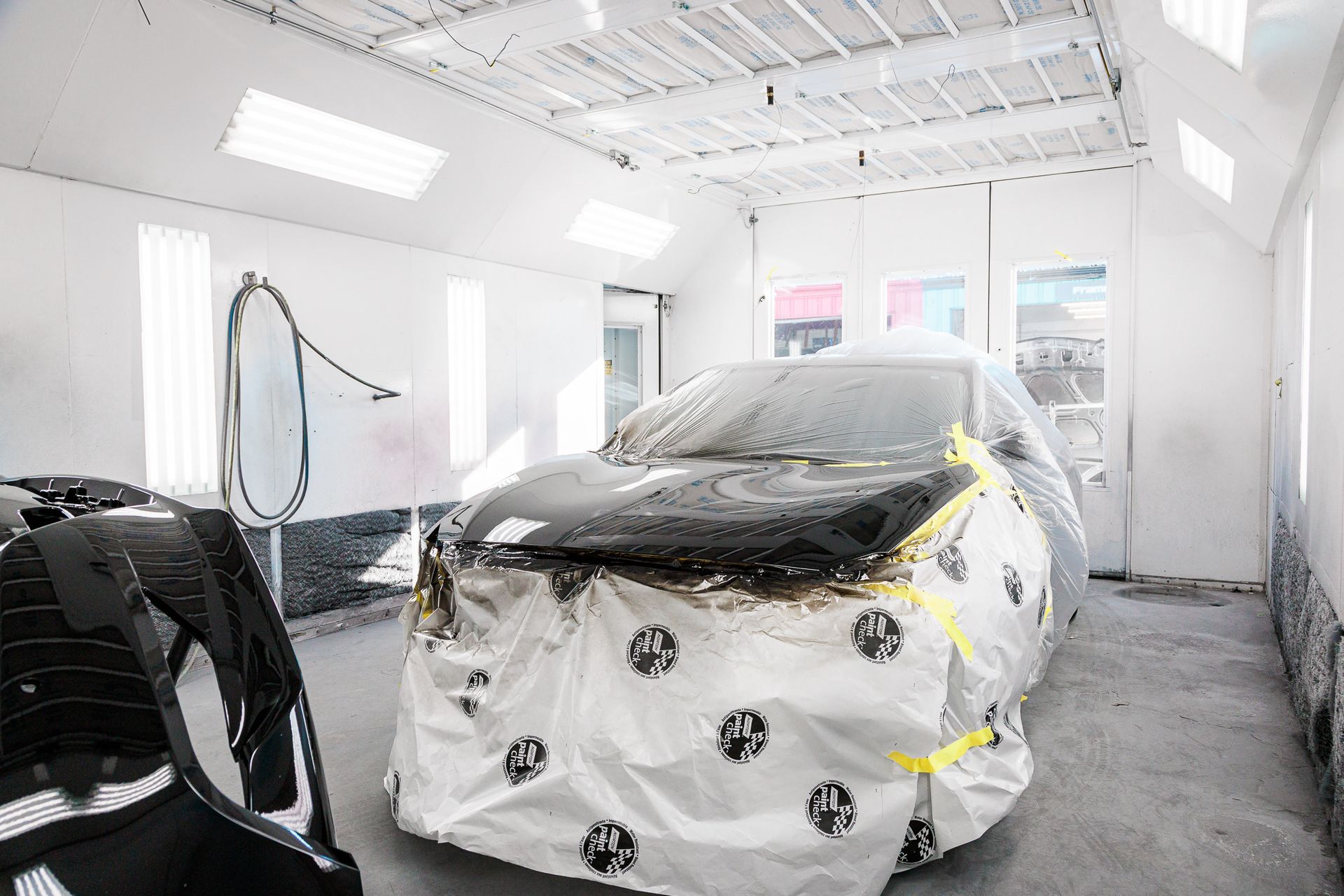 A car is covered in plastic in a paint booth.