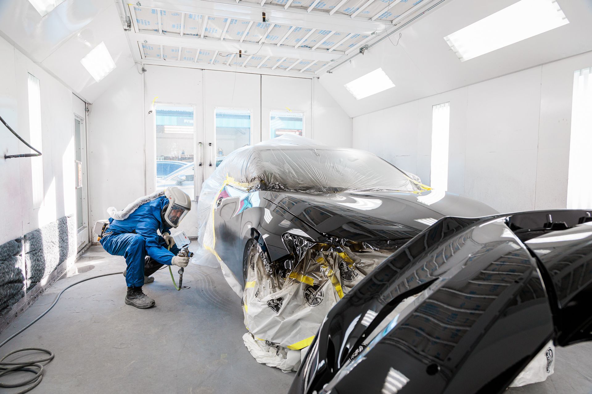 A man is painting a car in a paint booth.