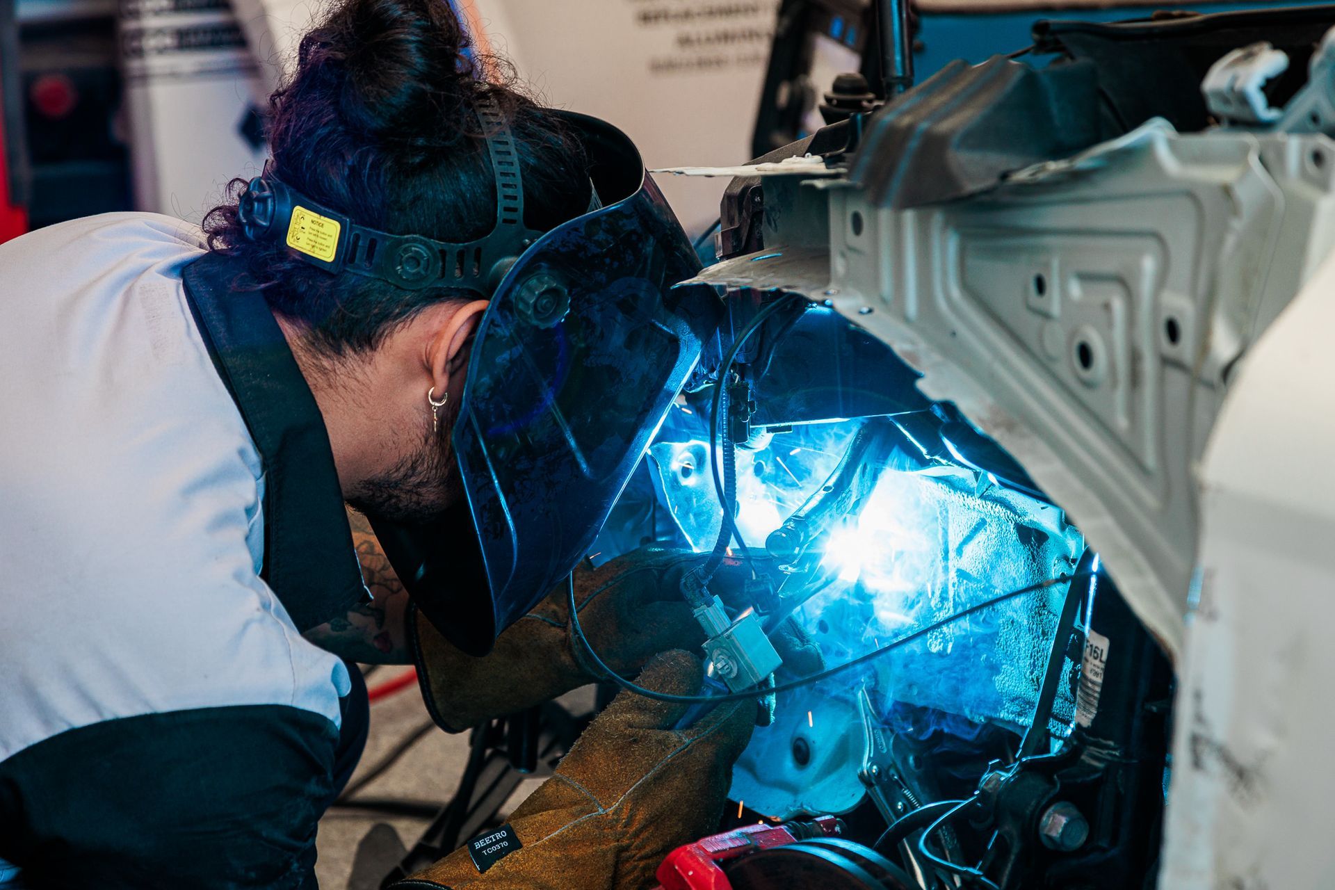 A man wearing a welding mask is working on a car.