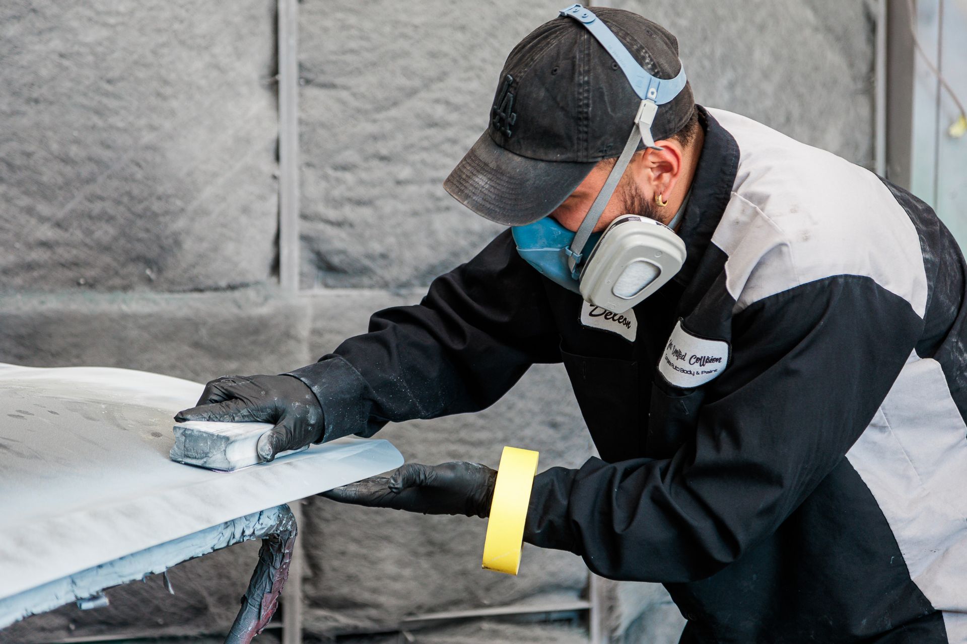 A man wearing a mask is sanding a piece of metal.