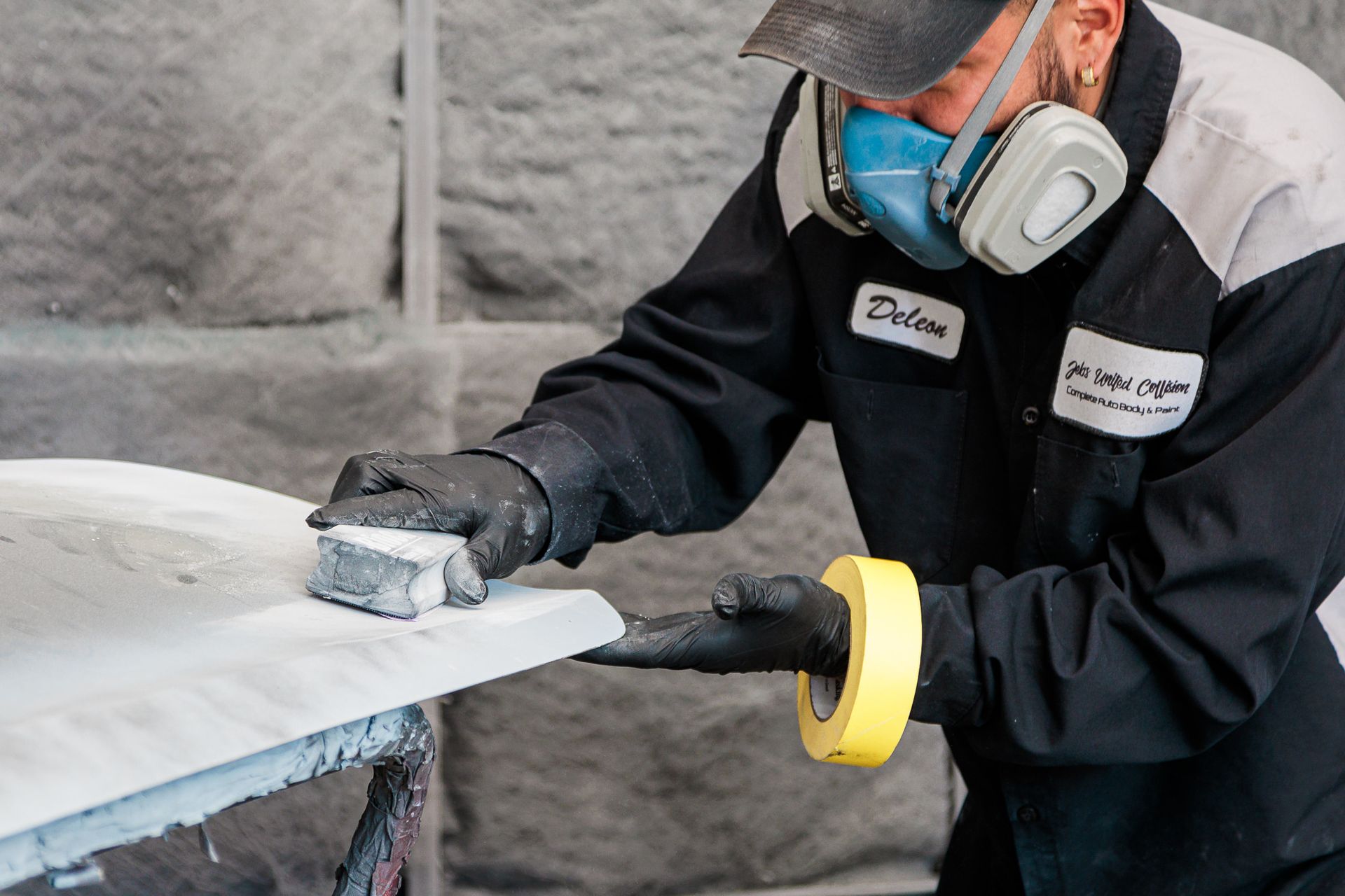 A man wearing a mask and gloves is sanding a piece of plastic.