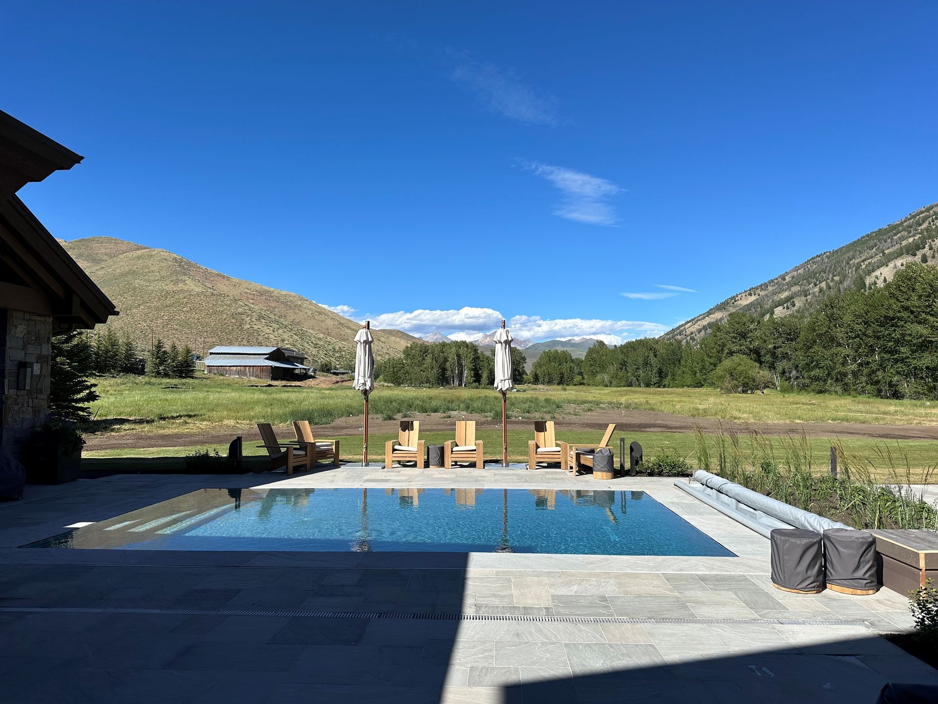 A large swimming pool surrounded by chairs and umbrellas with mountains in the background.