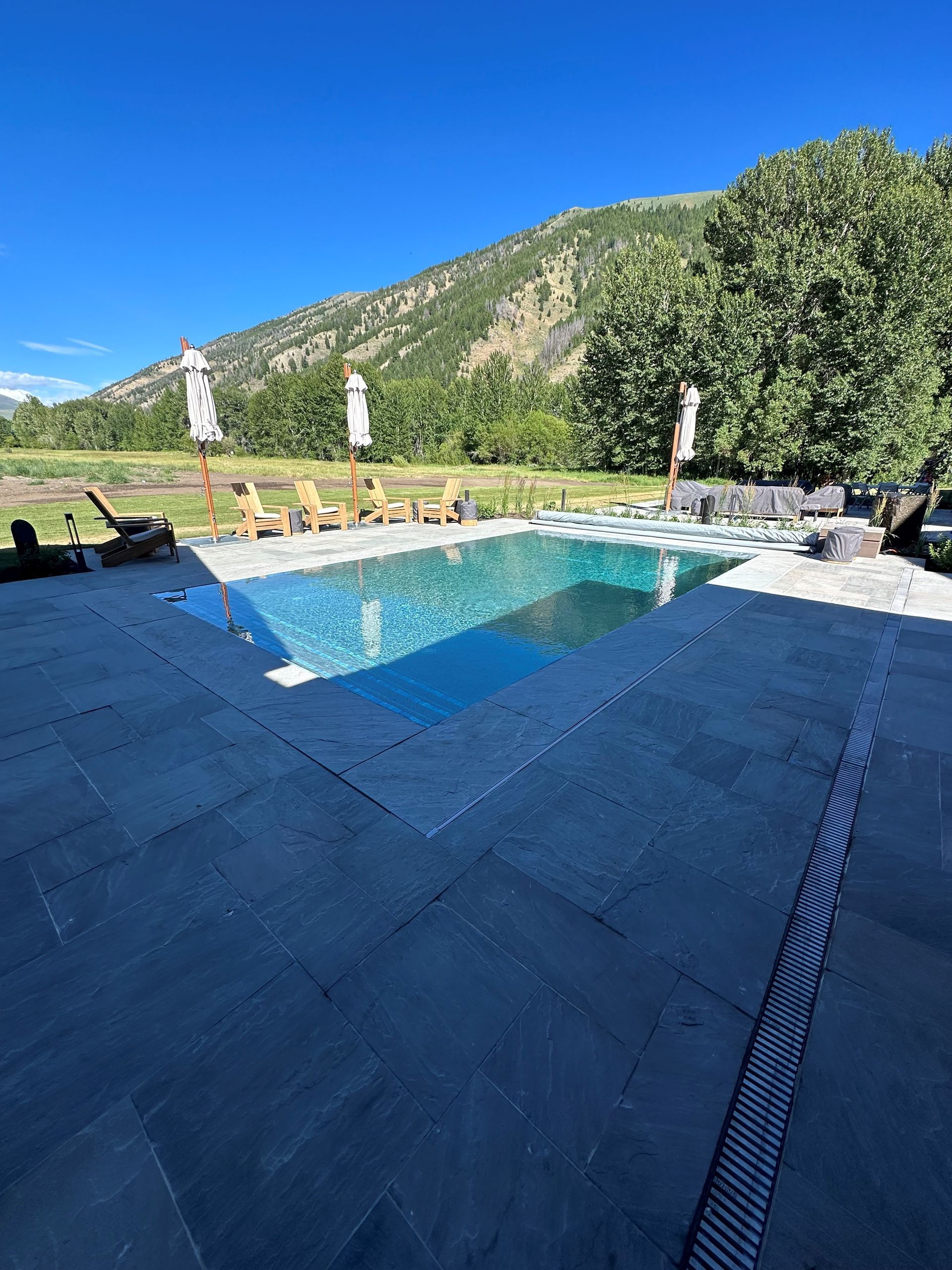 A large swimming pool surrounded by chairs and umbrellas with mountains in the background.