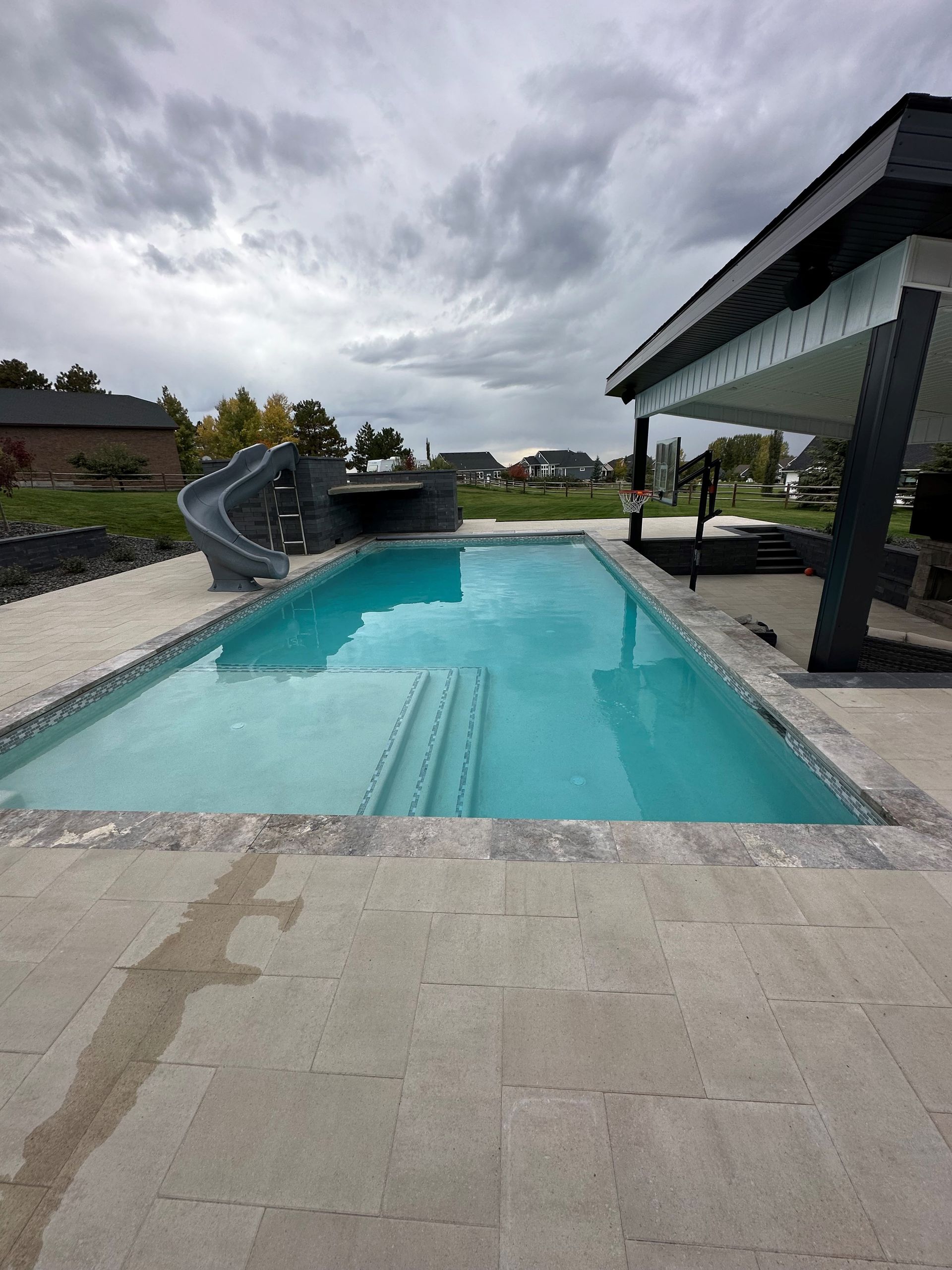 A large swimming pool with a slide in the backyard of a house.