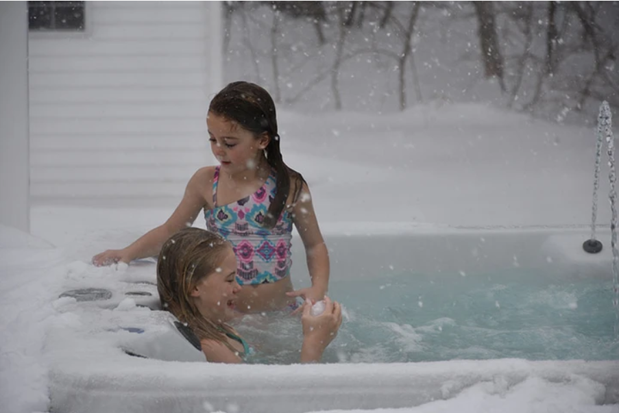 Two young girls are playing in a hot tub covered in snow.