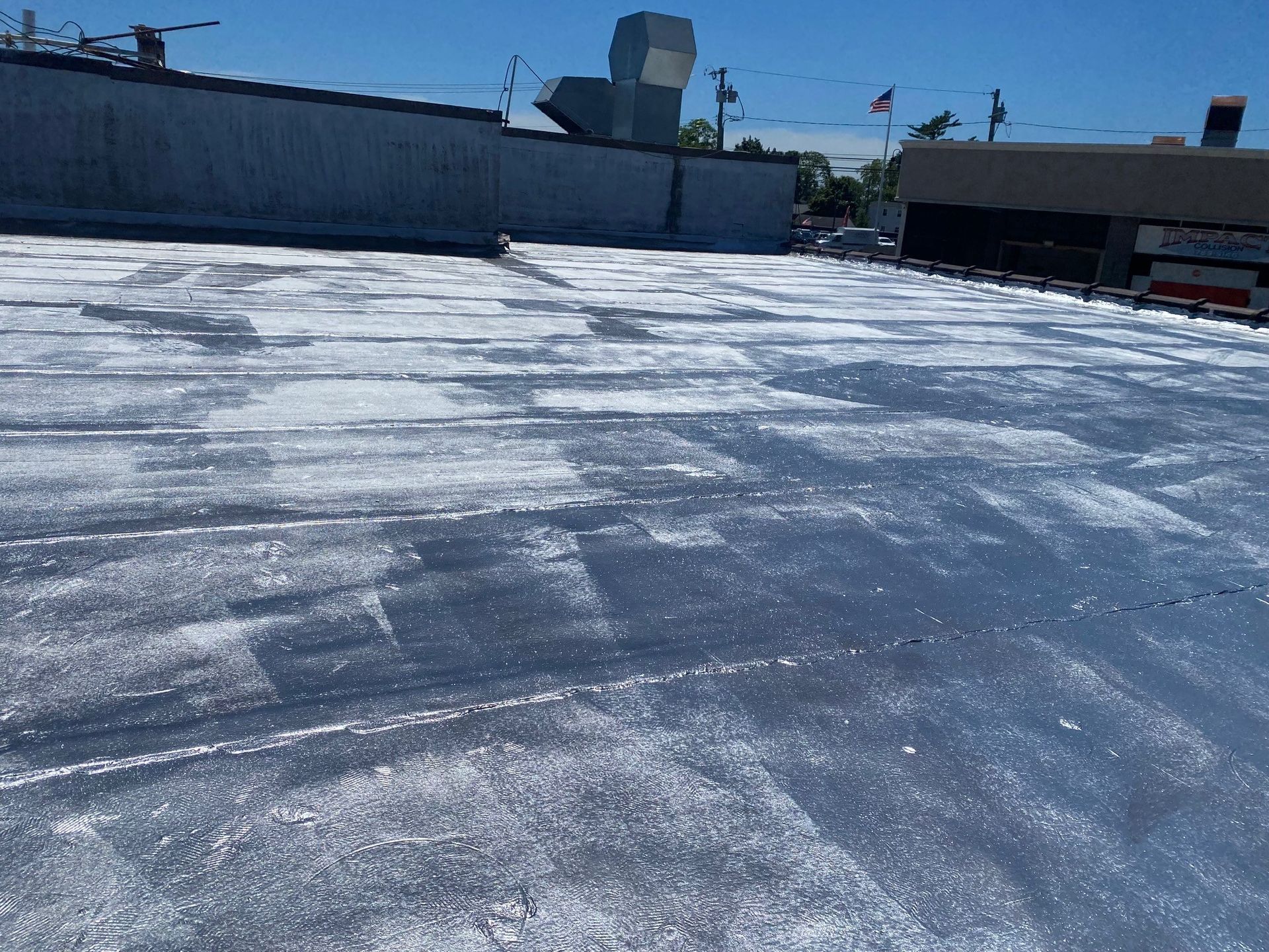 Rooftop with a reflective white coating under a bright blue sky, with buildings along the edge