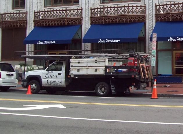 Utility truck parked by storefronts with blue awnings and orange traffic cones on the street